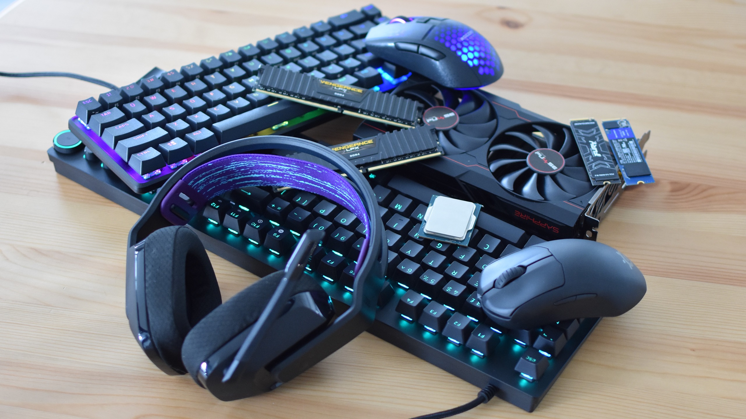 Assorted PC gaming hardware, including various keyboards, RAM sticks, SSDs and gaming mice, piled up on a table.