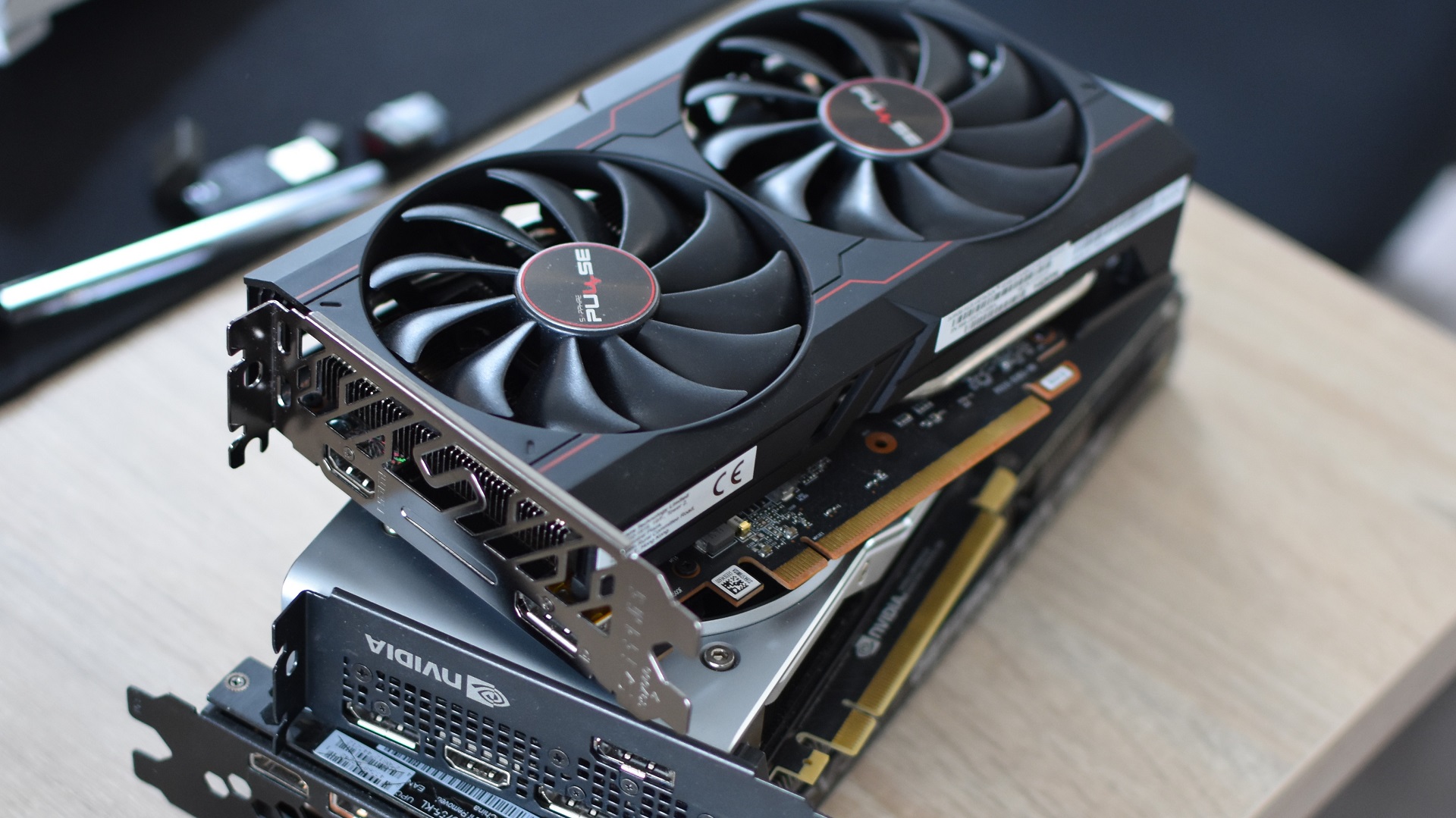 A stack of various Nvidia and AMD graphics cards, piled up on a desk.