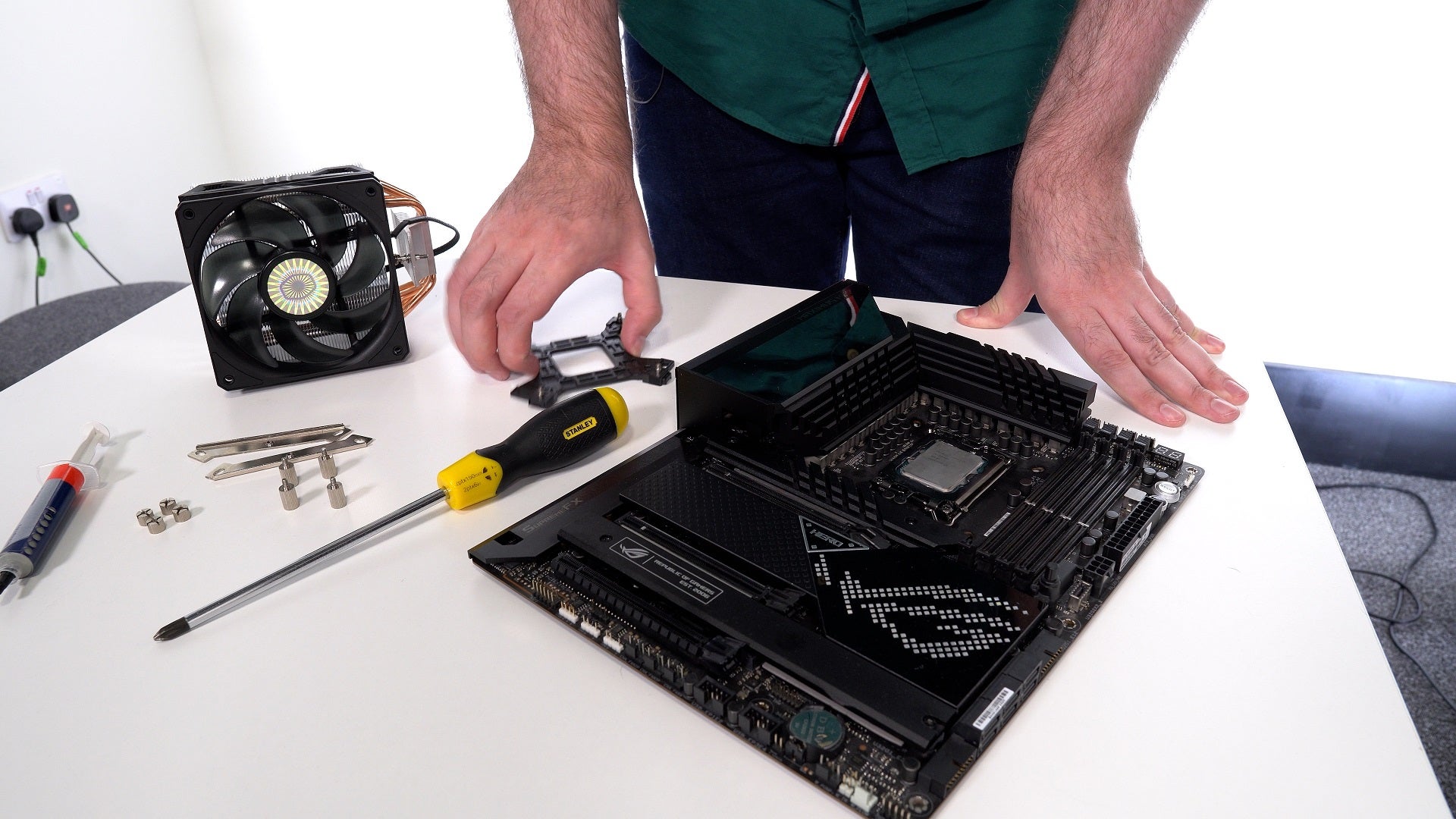 A motherboard (with CPU installed) sits on a table next to a screwdriver and CPU cooler, waiting to be installed.