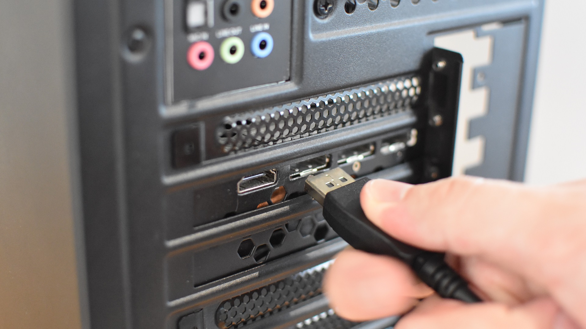 Connecting a DisplayPort cable to the rear outputs of a graphics card, which has been installed inside a gaming PC.