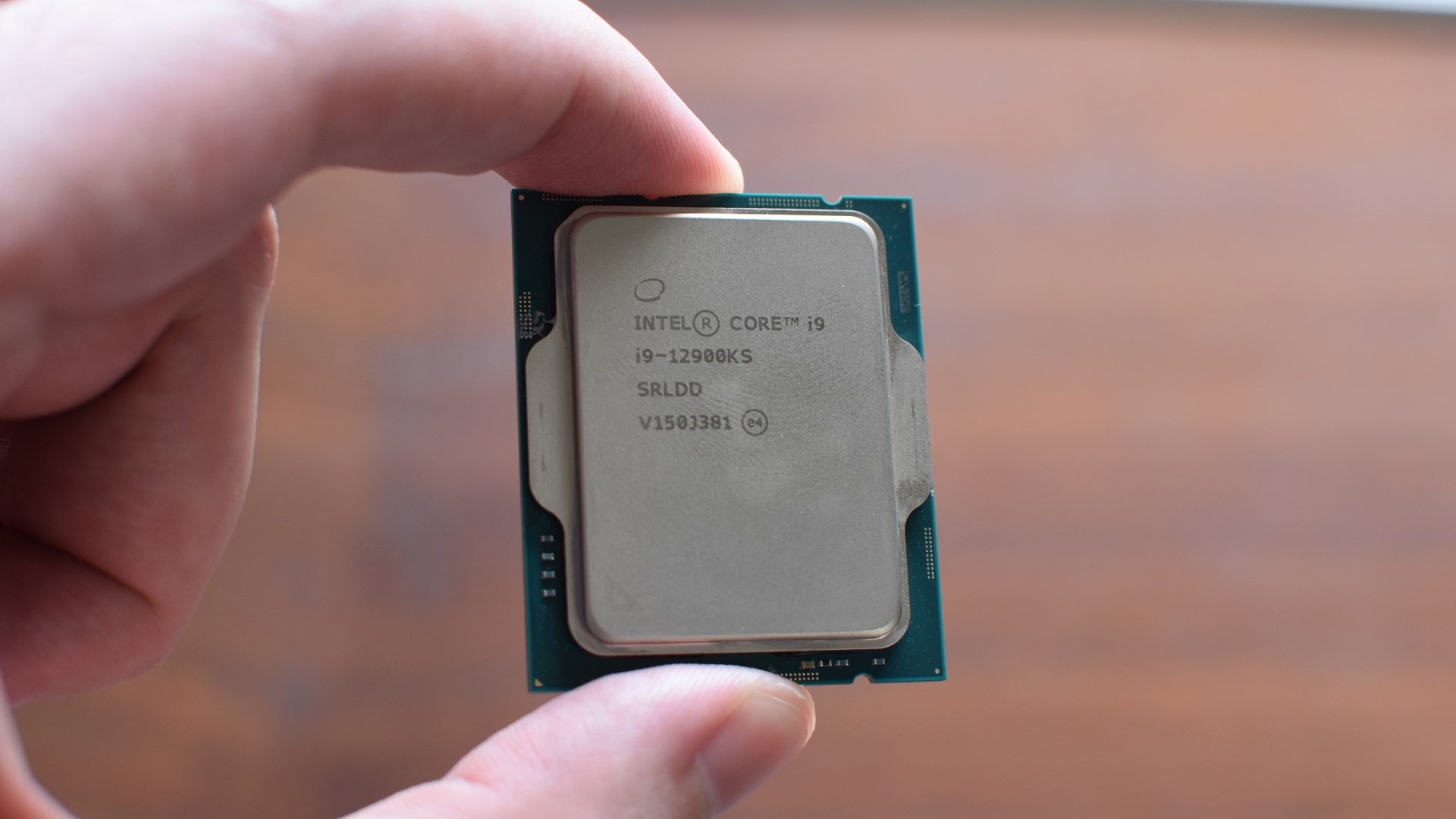 An Intel Core i9-12900KS processor held between a finger and a thumb.