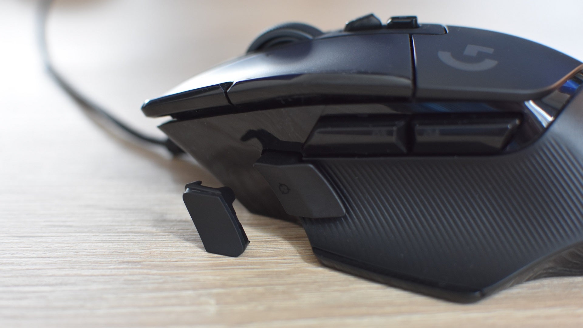 Un primer plano del botón de embrague DPI en el mouse para juegos Logitech G502 X, con su accesorio de cubierta simple junto a él en el escritorio.