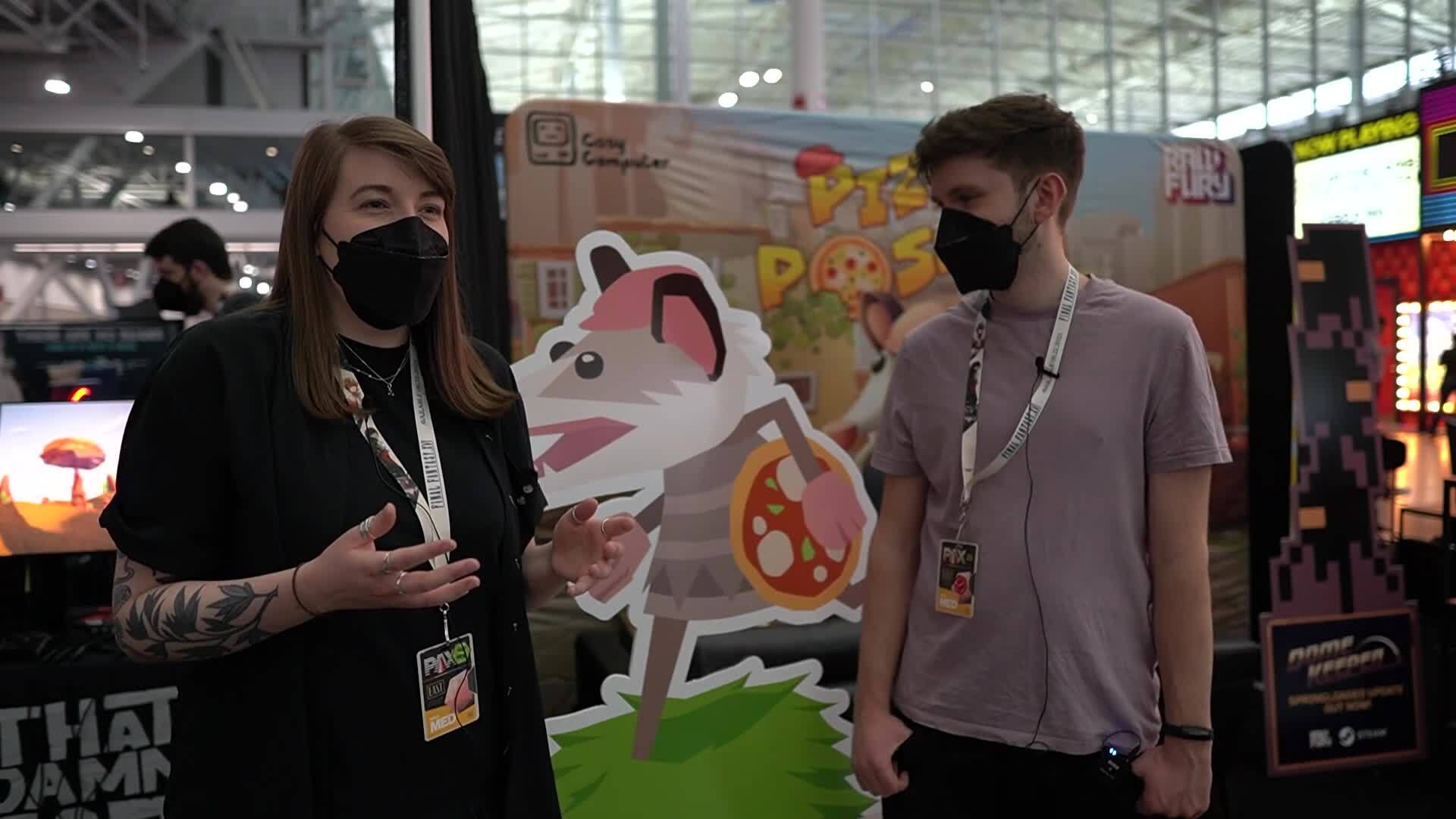 Liam and Rachel stand next to the Pizza Possum booth at PAX East