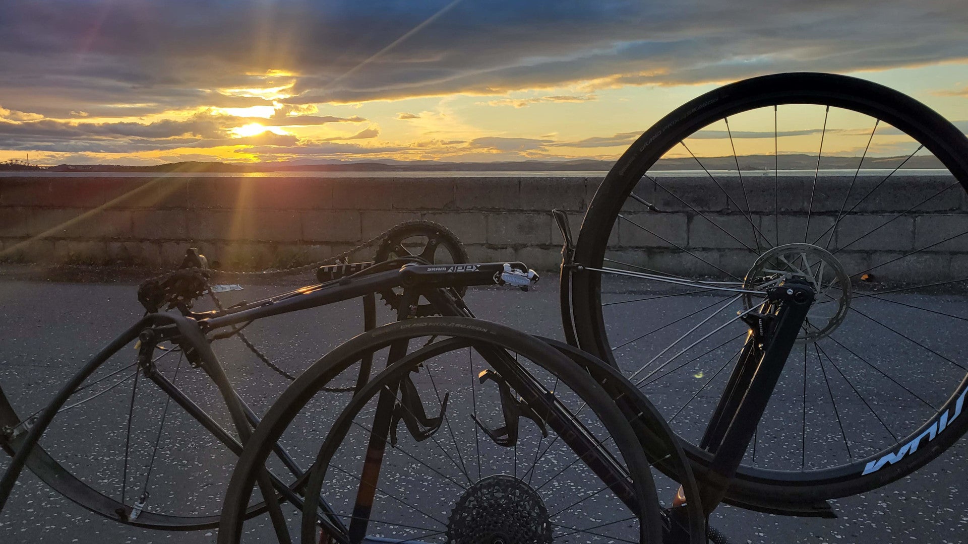A photo of an upside-down bicycle with the back wheel off, backlit by a sunset.