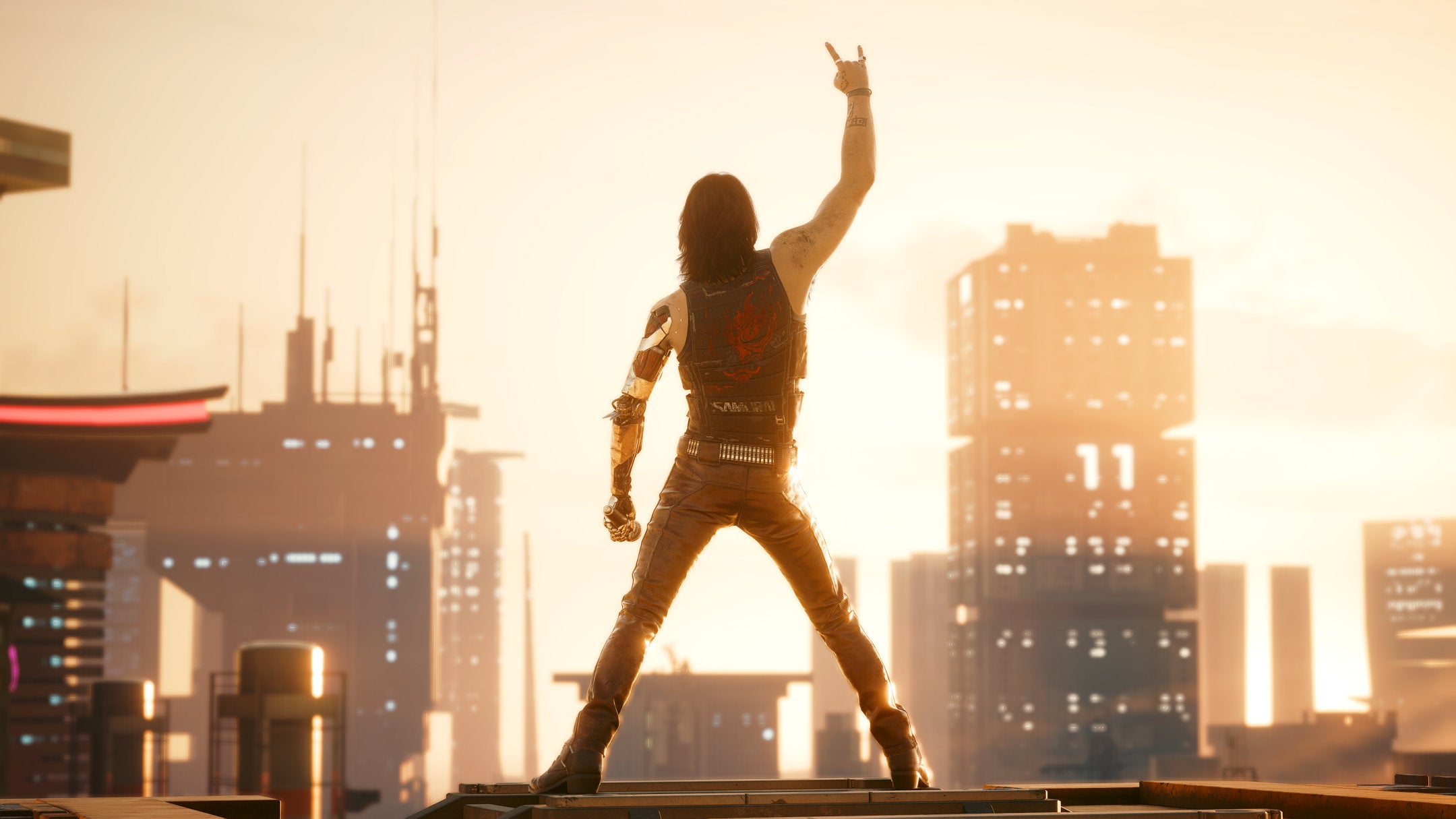 Johnny Silverhand, a character in Cyberpunk 2077, poses with his back to the camera, facing the skyline of Night City.