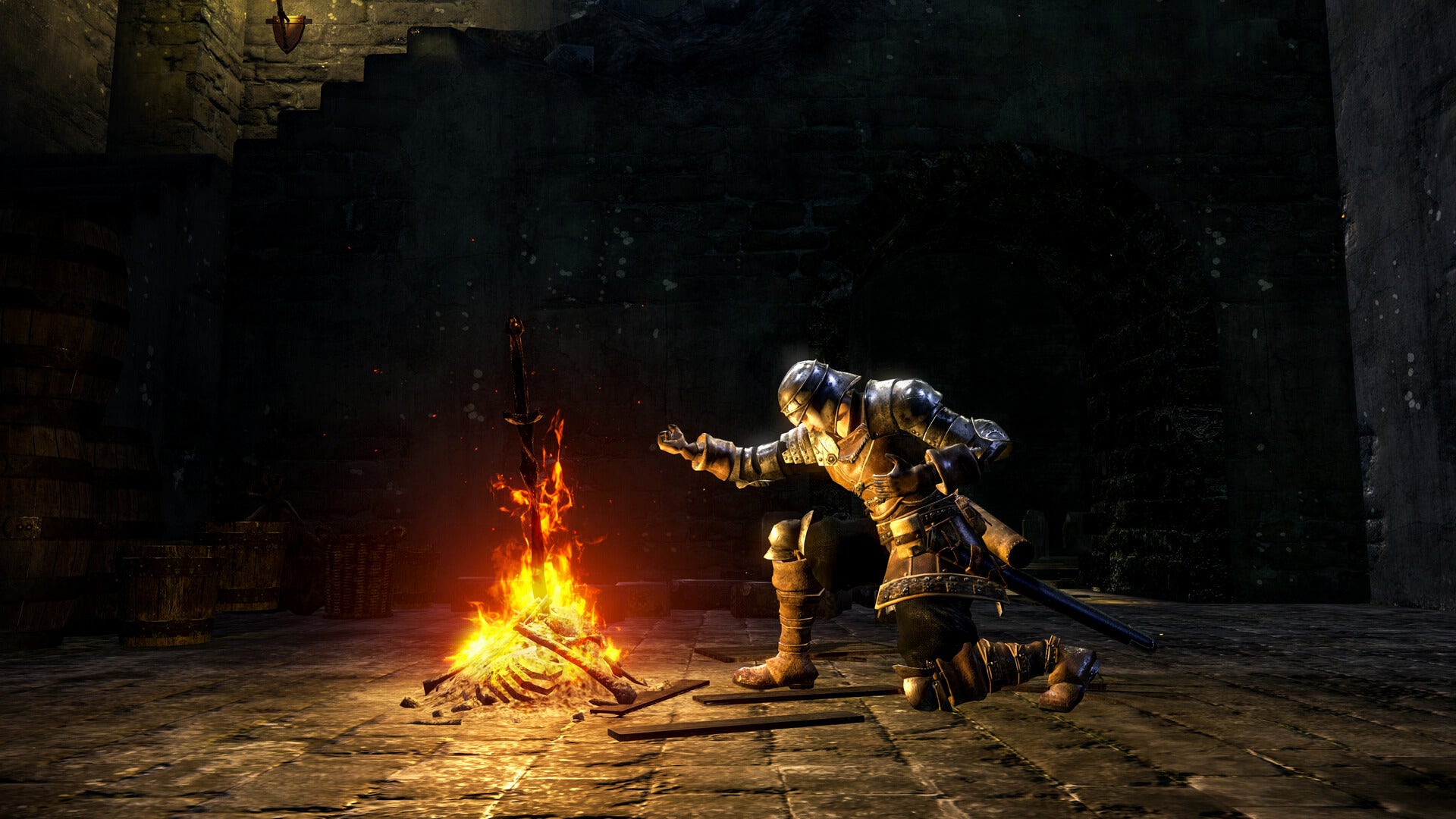O personagem do jogador em Dark Souls, um cavaleiro vestido de armadura, ajoelha-se diante de uma fogueira