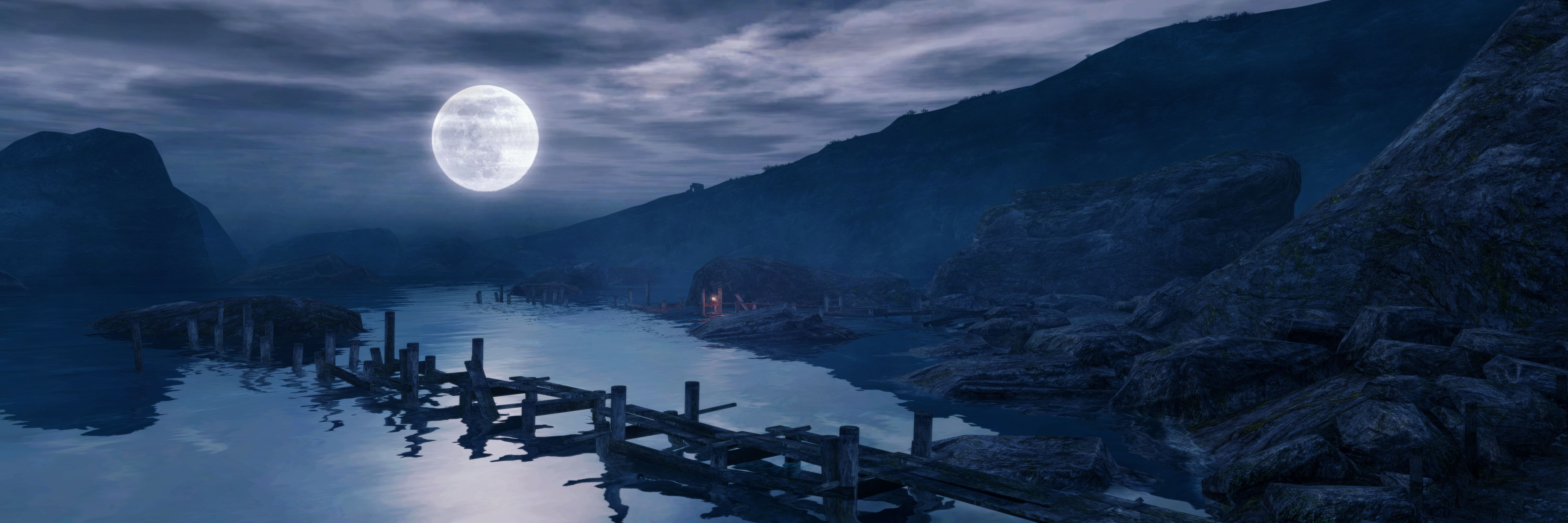 A wide shot of a night time landscape from Dear Esther, a huge moon lighting a small rocky beach, with the bones of a wooden jetty sticking out of the water in the foreground