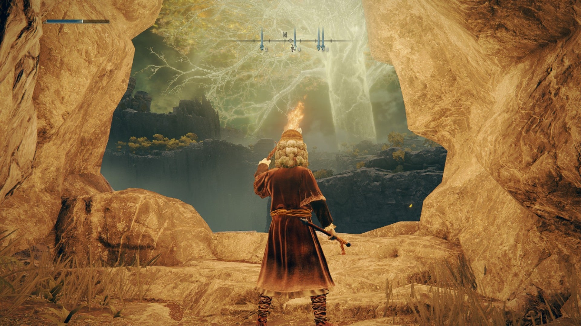 Elden Ring player holding a torch as they leave Coastal Cave, Great Erdtree towers in the horizon