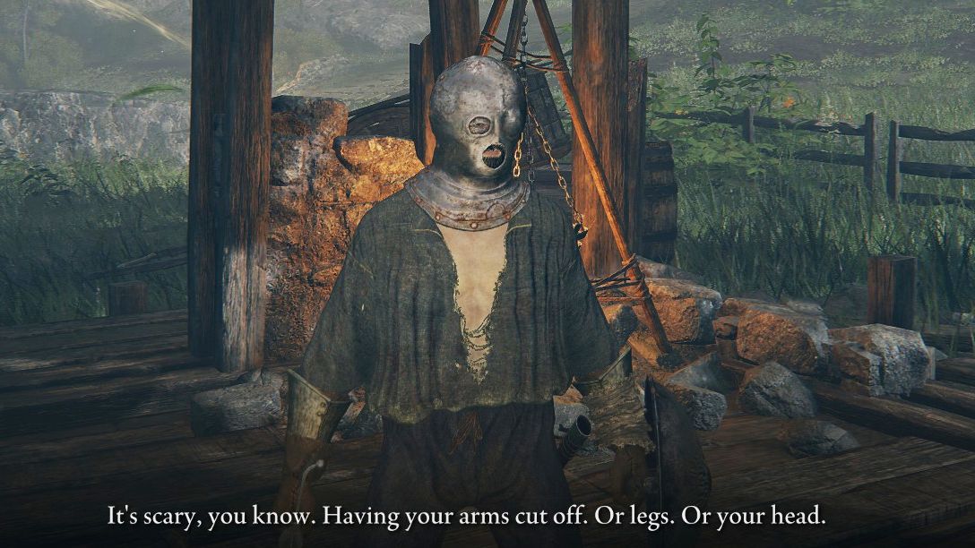 The player character in Elden Ring stands, dressed in rags and wearing an iron mask on their head, stands in a ruined house. An NPC, off screen, has said "It's scary you know. Having your arms cut off. Or legs. Or your head."