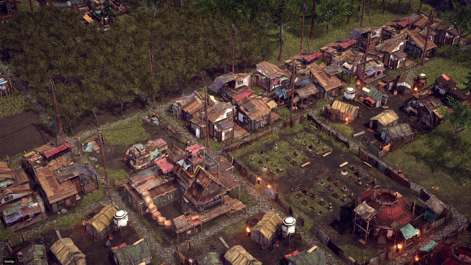 A screenshot of Endzone: A World Apart, showing from above some grass and trees and a lot of ramshackle houses built from repurposed wood and metal materials.
