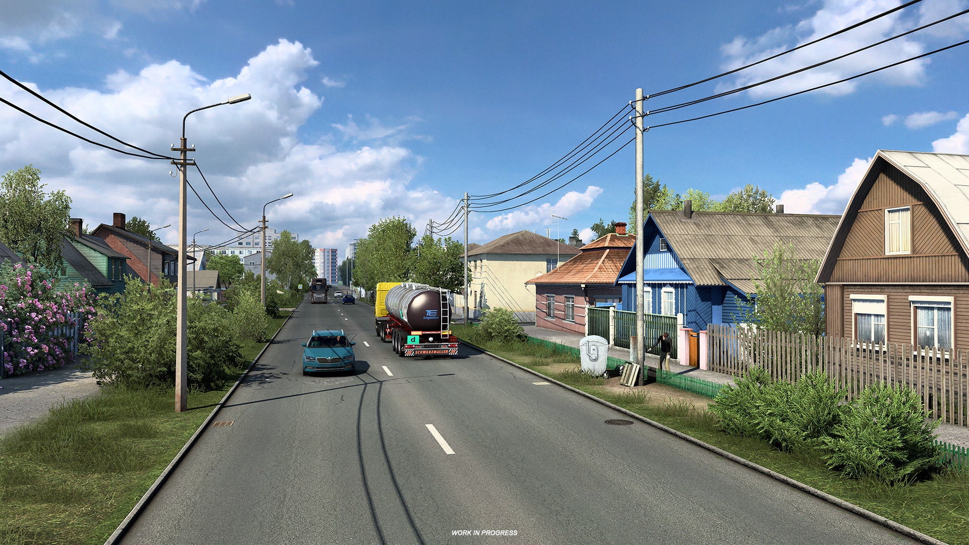 Euro Truck Sim 2 Russia - Trucks and cars drive on a two lane road between rows of colorful houses.
