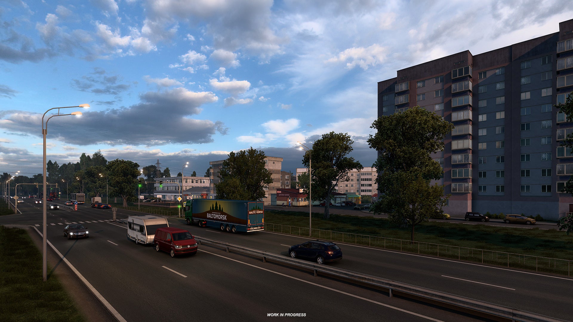 Euro Truck Sim 2 Russia - Cars and trucks on a four lane road drive past tall buildings and apartments at sunset.