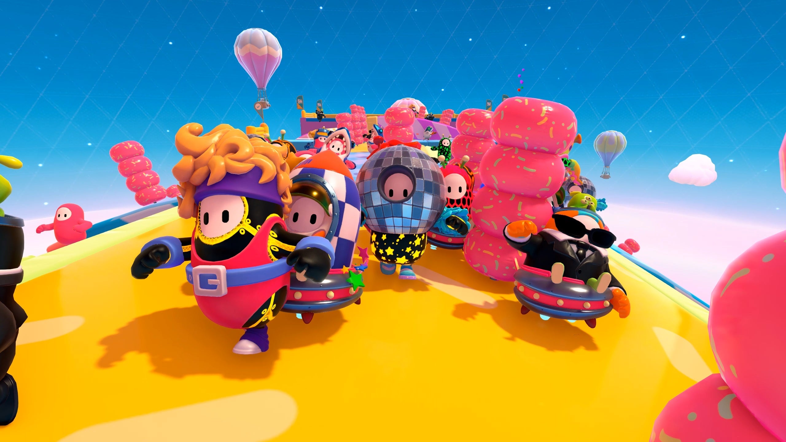 Several Fall Guys race along the new Roll On level, a large, rotating cylinder. They're all wearing new 80's inspired costumes such as a disco ball hat and a pink leotard with a belt and headband.