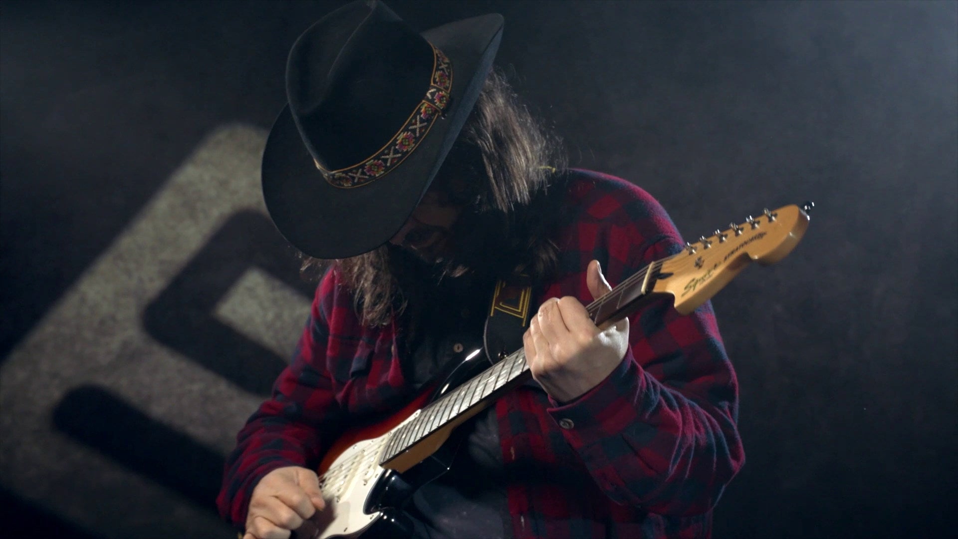 A man in a cowboy hat and flannel shirt plays electric guitar in a Farming Simulator 19 DLC trailer.