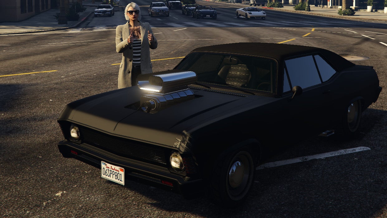 A woman does a thumbs-up gesture while standing behind a muscle car with a giant supercharger in a GTA Online screenshot.