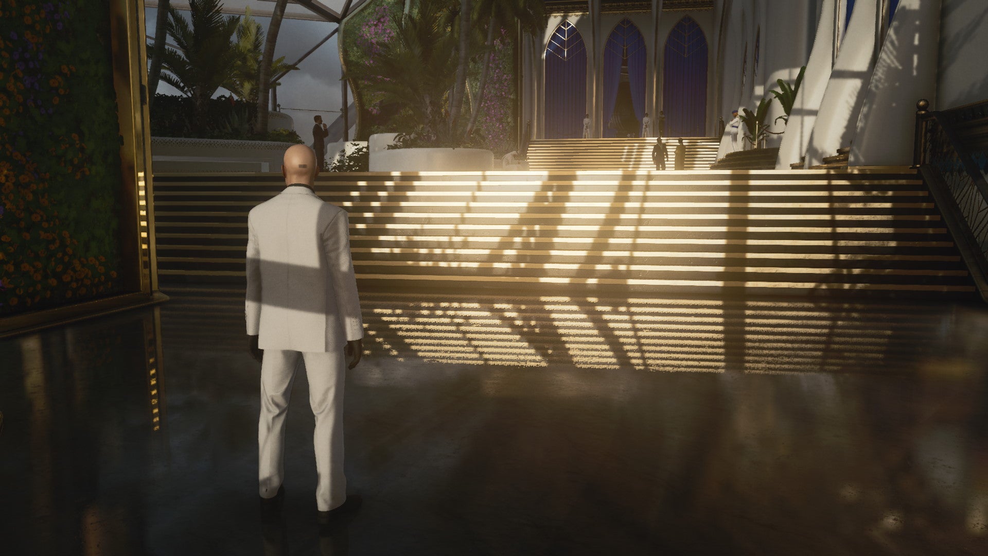 A screenshot of Agent 47 standing in front of a shiny set of stairs in Hitman 3's Dubai level
