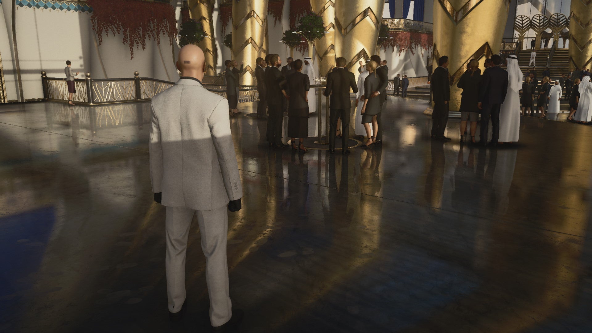 A screenshot of Agent 47 standing in a shiny reception hall from Hitman 3's Dubai level
