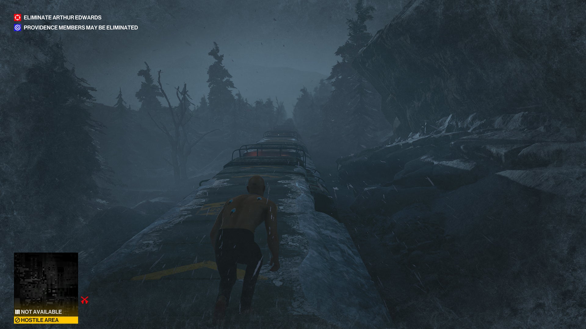 Ian Hitman is crouched on top of an icy train moving through a dark forested landscape, in the Carpathian Mountains level - the final of the trilogy.