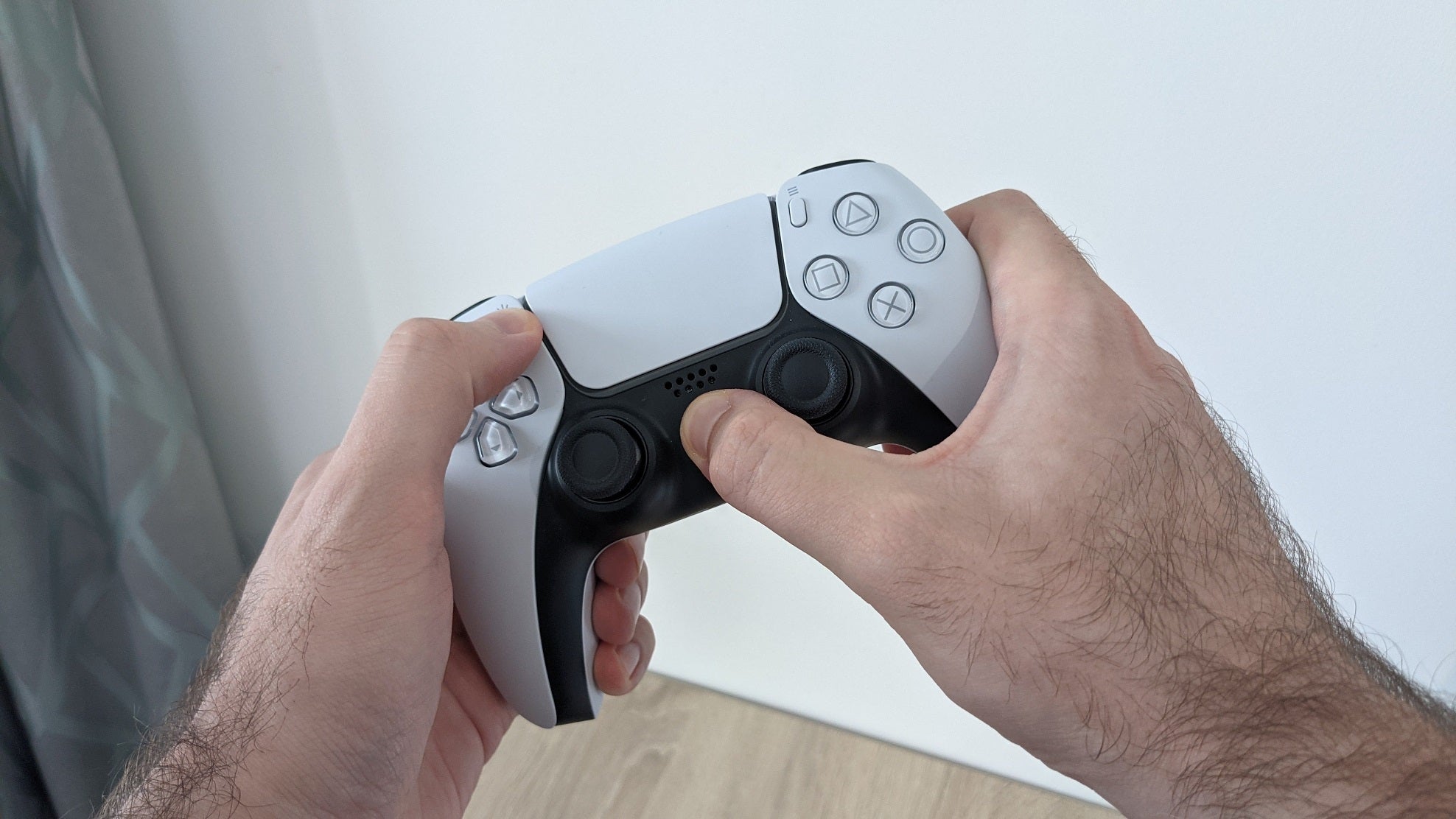 A PS5 controller, with the user's hands holding down the PS and Share buttons to initiate Bluetooth pairing.