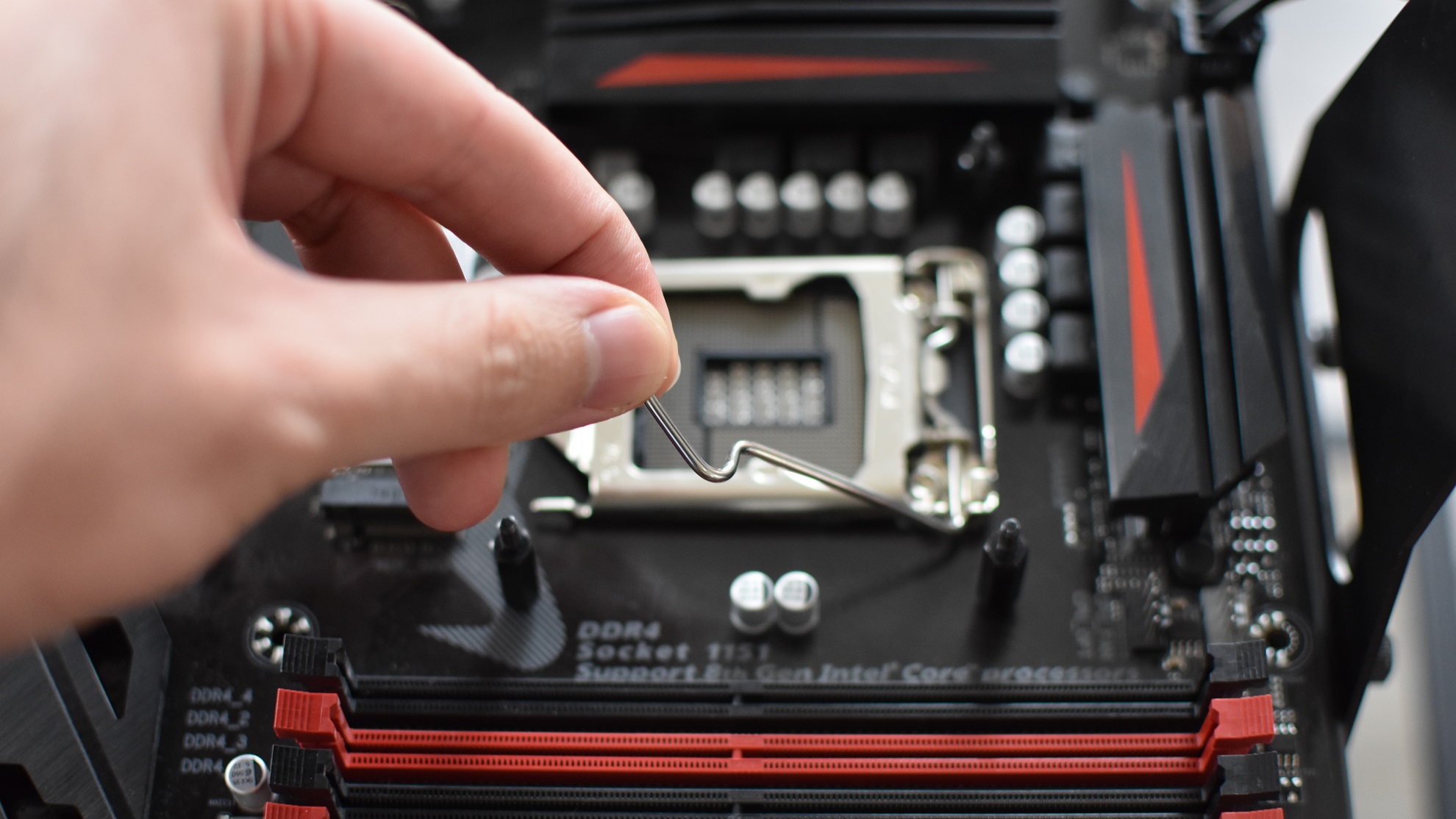 A hand lifts the locking arm on a motherboard's Intel LGA 1151 socket.