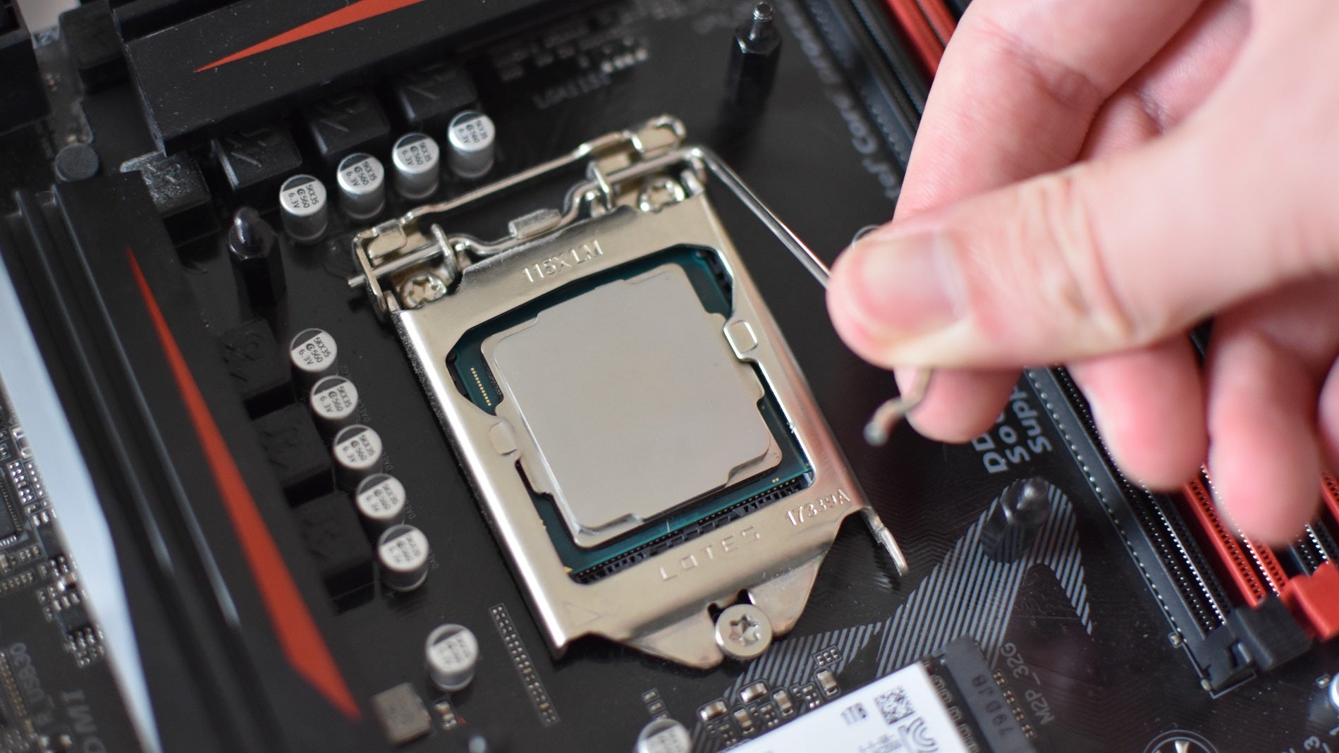 A hand pressing down on the locking arm of an Intel LGA 1151 motherboard socket, with an Intel CPU installed within.