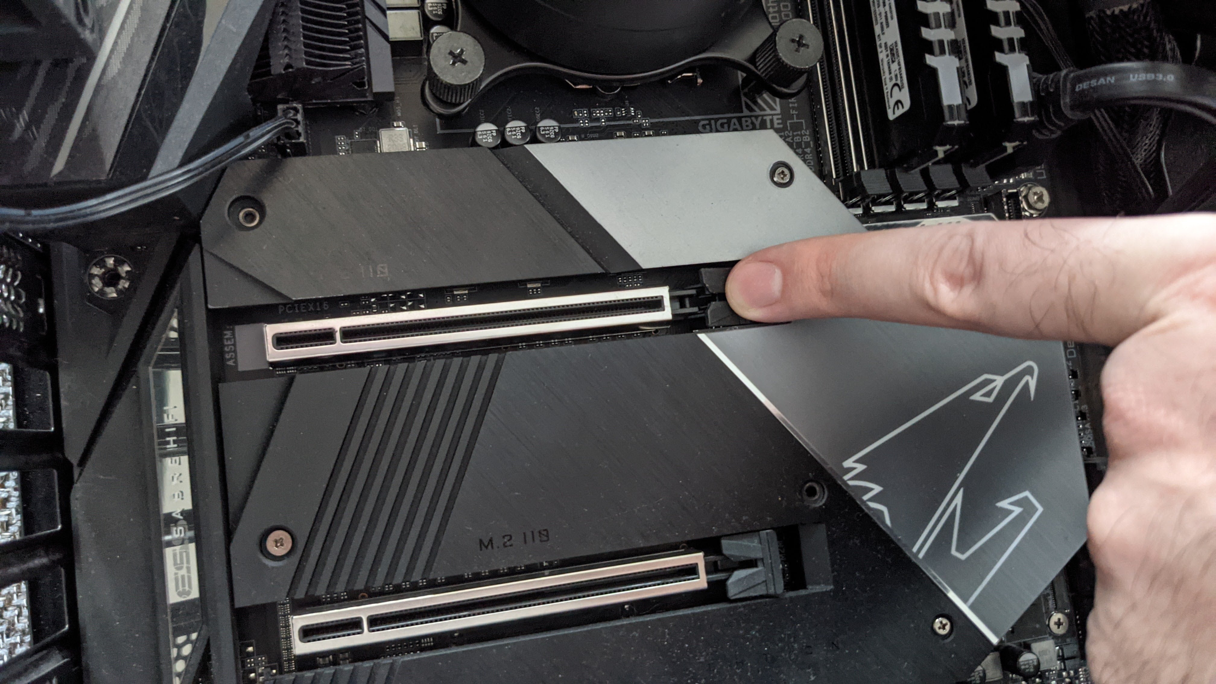 A finger presses down on the release latch of a motherboard's PCIe x16 slot.