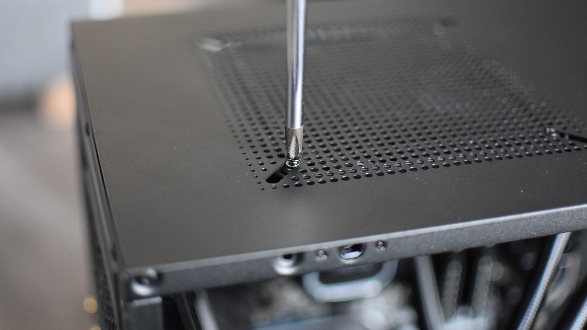 A screwdriver tightens one of four mounting screws on a PC case fan.