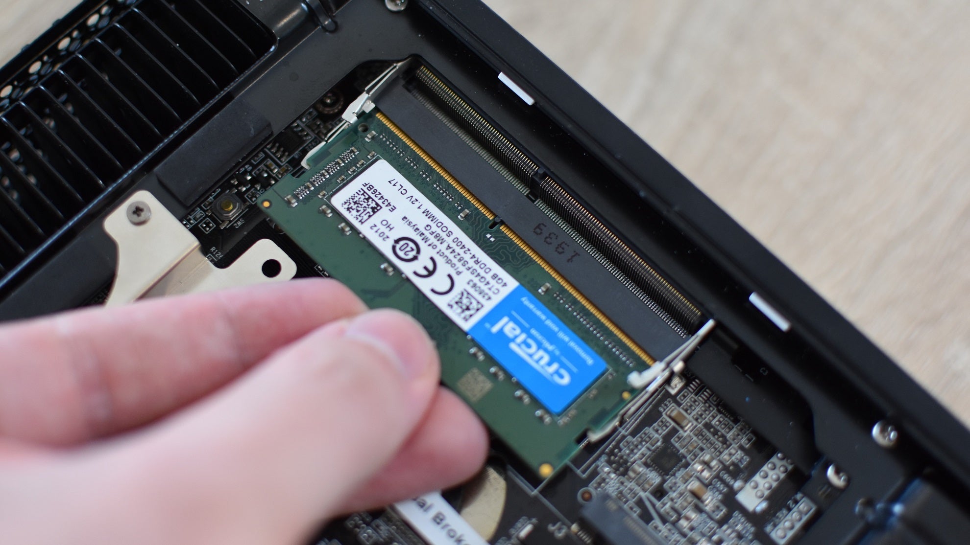 A stick of SO-DIMM RAM being pushed into a memory slot inside a mini-PC.