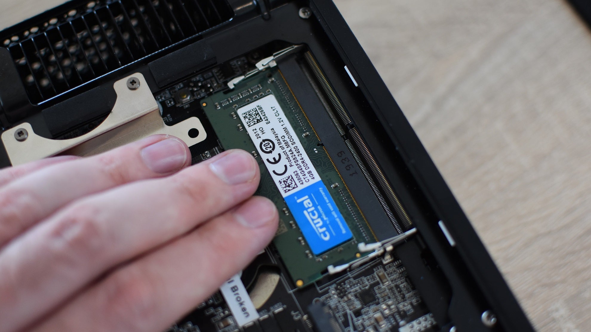 A hand pressing down onto a stick of SO-DIMM RAM, locking it in place inside its motherboard slot.