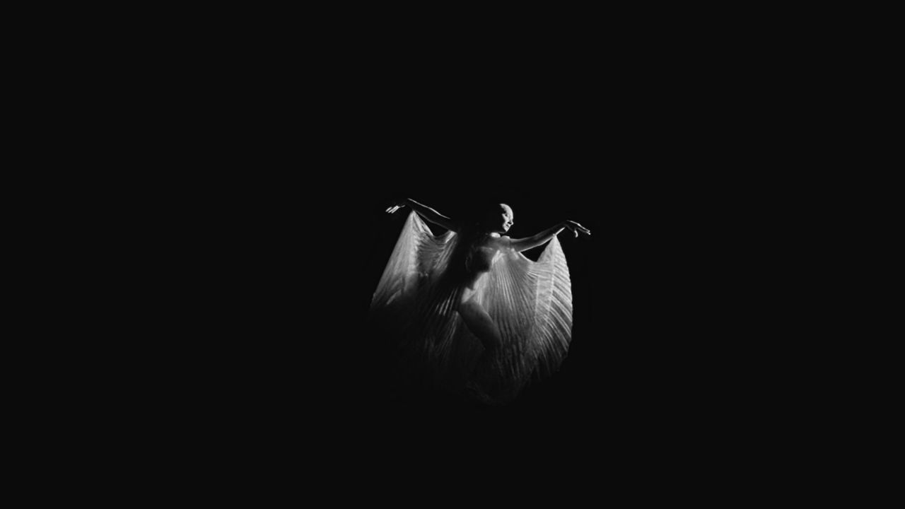 Una mujer baila con una capa flotante transparente, en un vacío negro, de un clip de Immortality