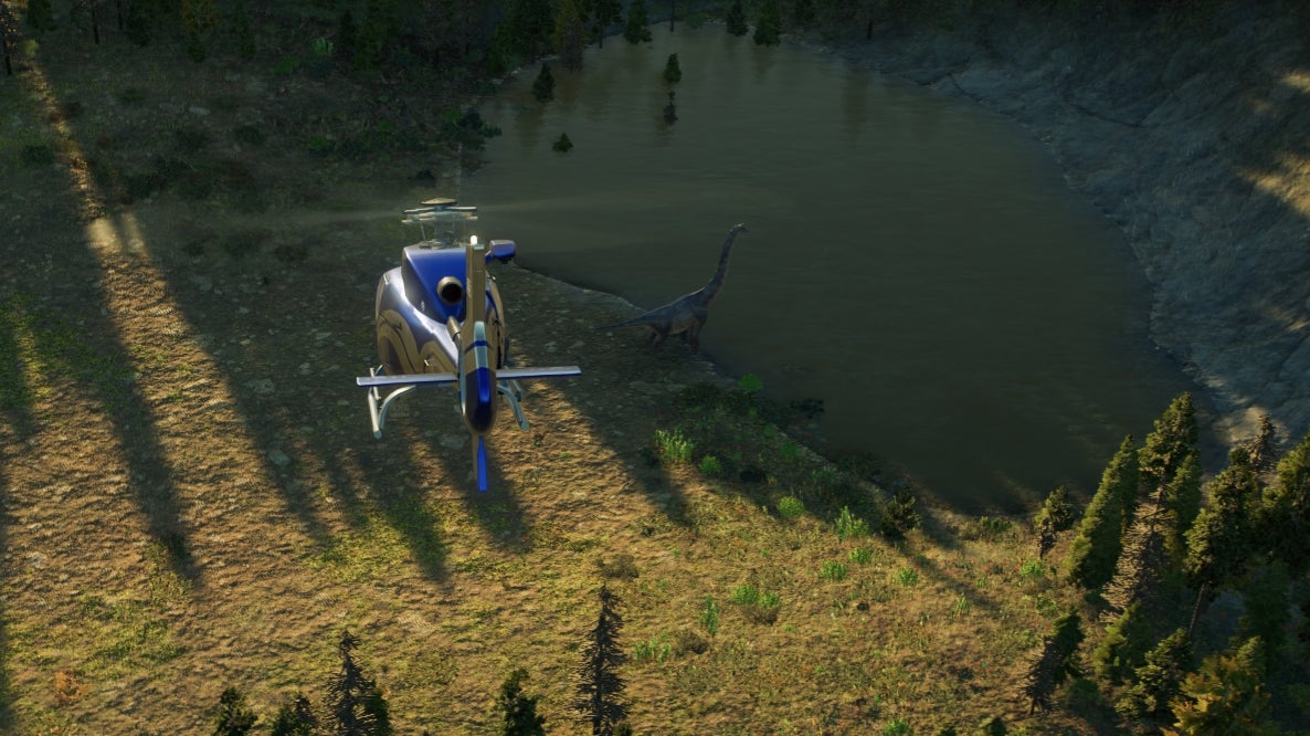 A screenshot from Jurassic World Evolution 2, where a helicopter is flying above and behind a large long-necked herbivore dinosaur, beside a small lake