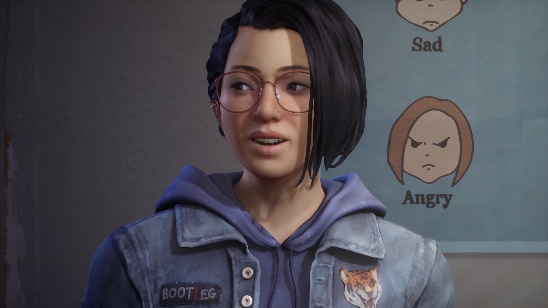 Life Is Strange: True Colors - Main character Alex Chen sits, talking, in front of a poster with drawn faces labeled "Sad" and "Angry"