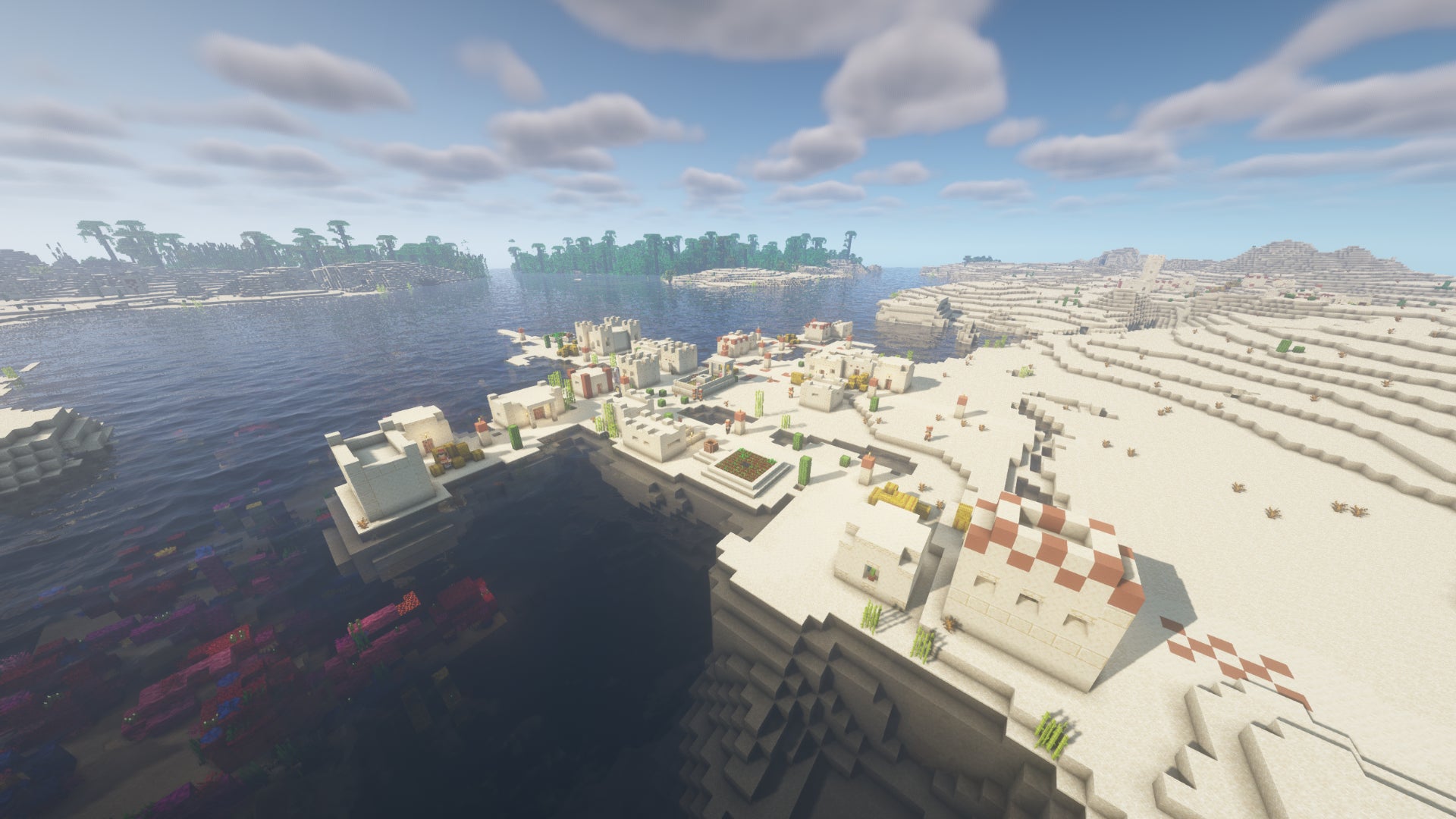 A Minecraft desert biome with a village in the foreground, and jungle in the distance across the water.