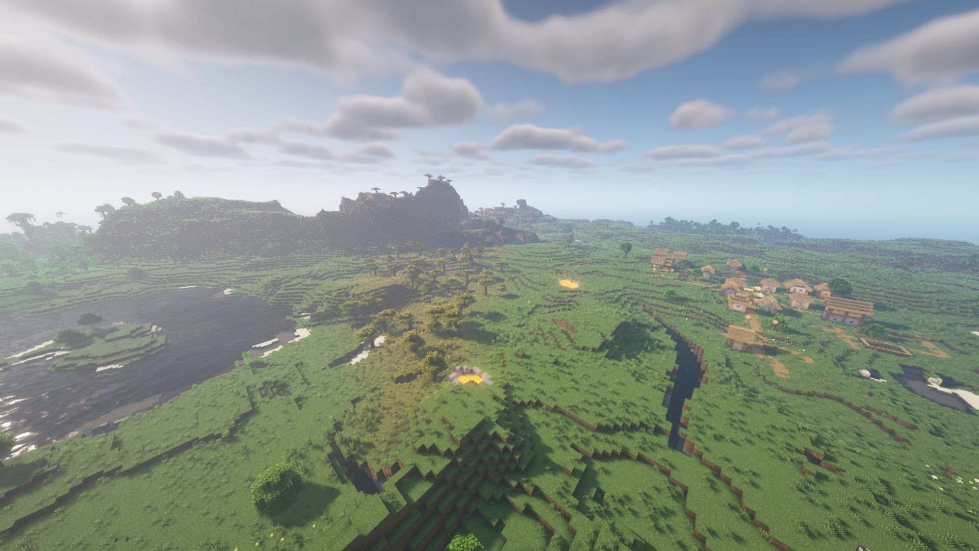 Un paysage Minecraft de plaines et de rivières, avec un village à droite et des montagnes à gauche au loin.