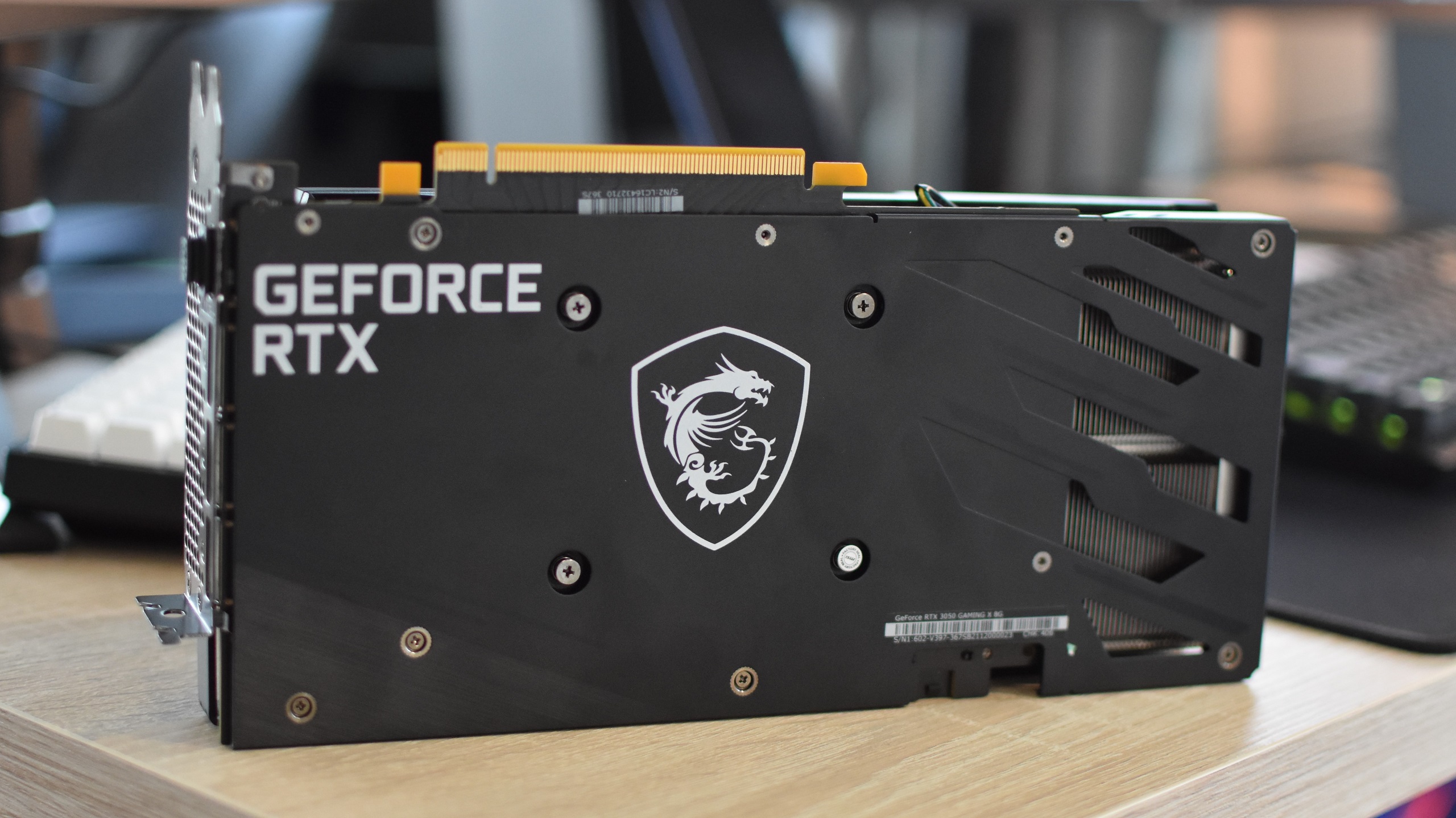 MSI GeForce RTX 3050 Gaming X 8G på ett skrivbord, som visar sin förstärkta bakplatta.