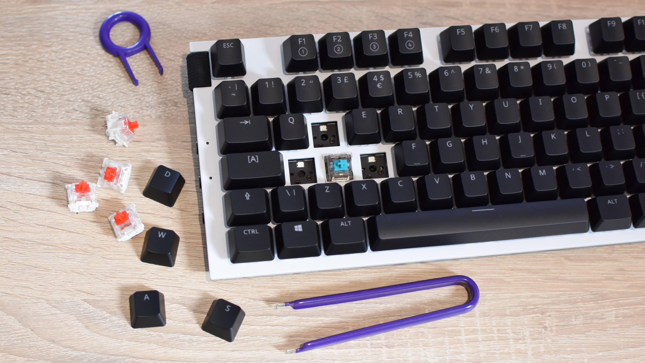 An NZXT Function gaming keyboard in the process of having its WASD key switches hot-swapped. Several removed keycaps and switches sit next to the keyboard, alongside some tools.