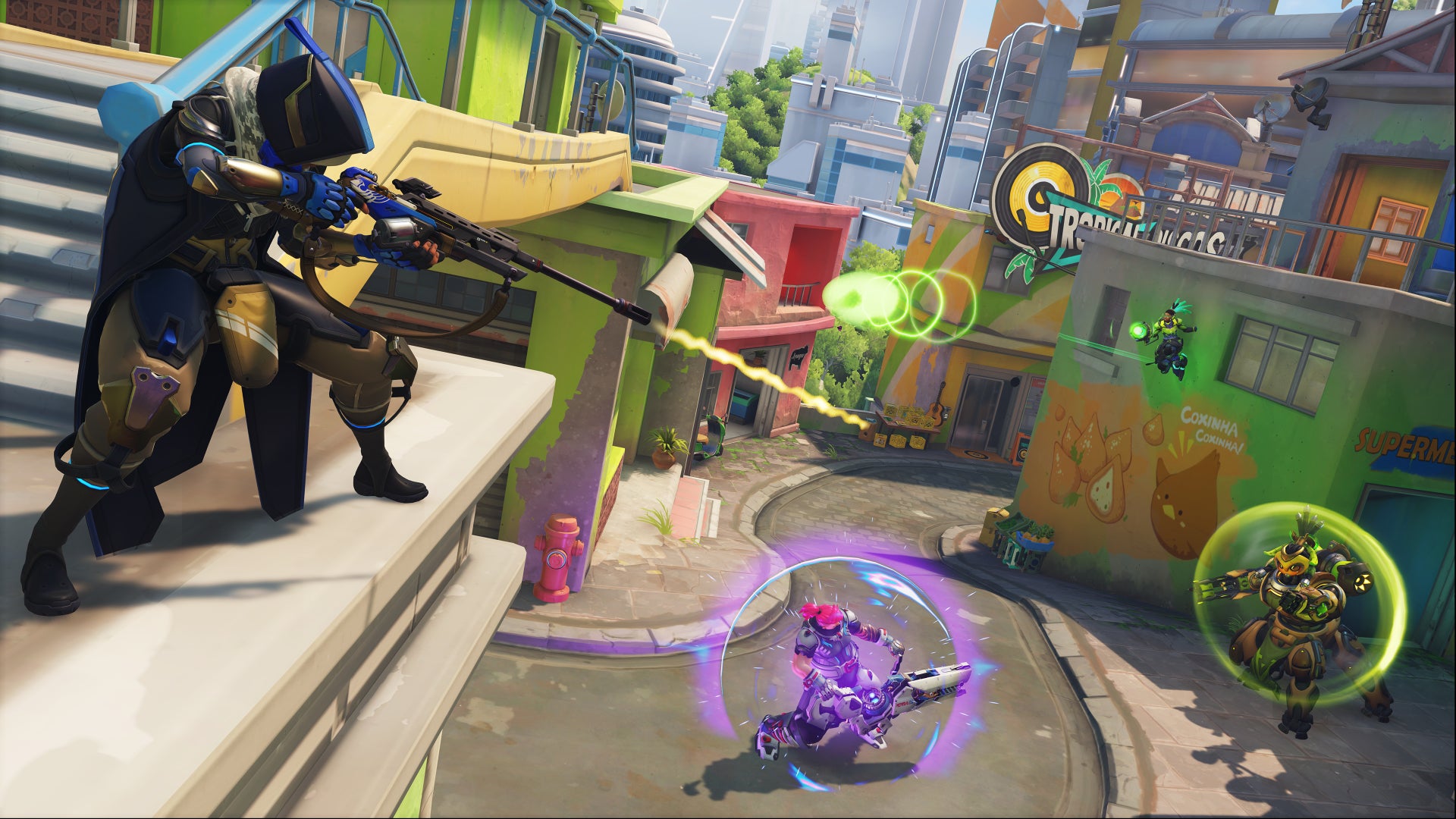 Ana, a hero in Overwatch 2, perches on a rooftop and shoots down at an Orisa, Lucio, and Zarya on the street below.