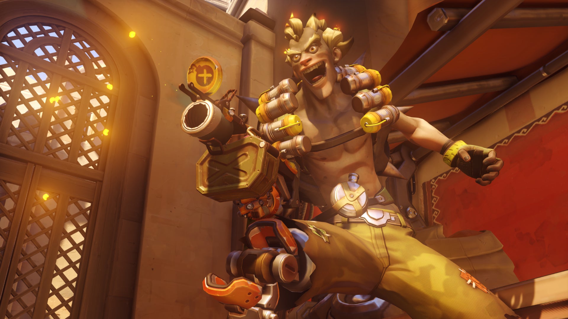 Junkrat, a hero in Overwatch 2, stands in front of the camera laughing and aiming his grenade launcher off-screen.