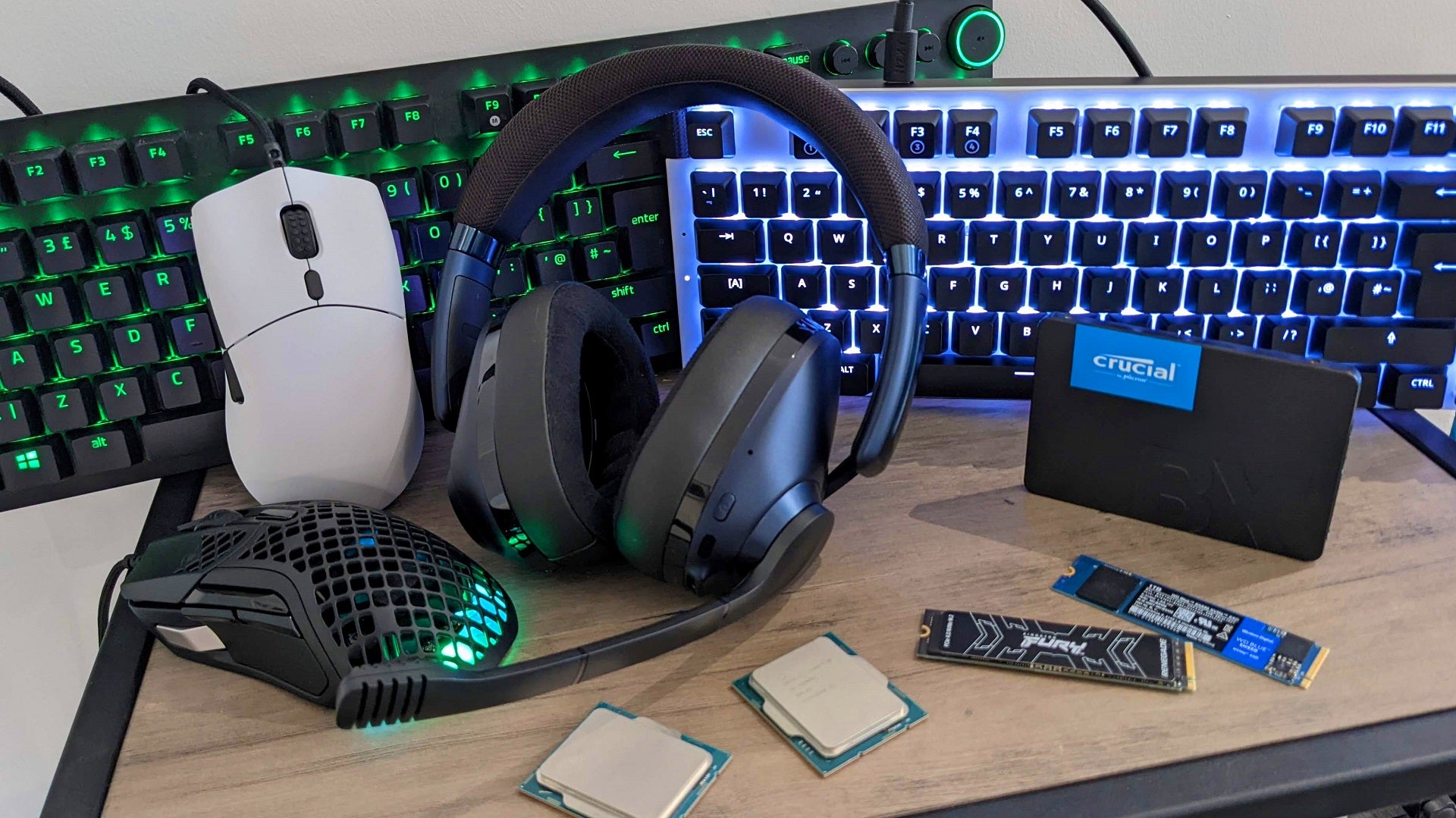 Various PC peripherals and peripherals on a table, including two keyboards, two mice, a headset and three SSDs.