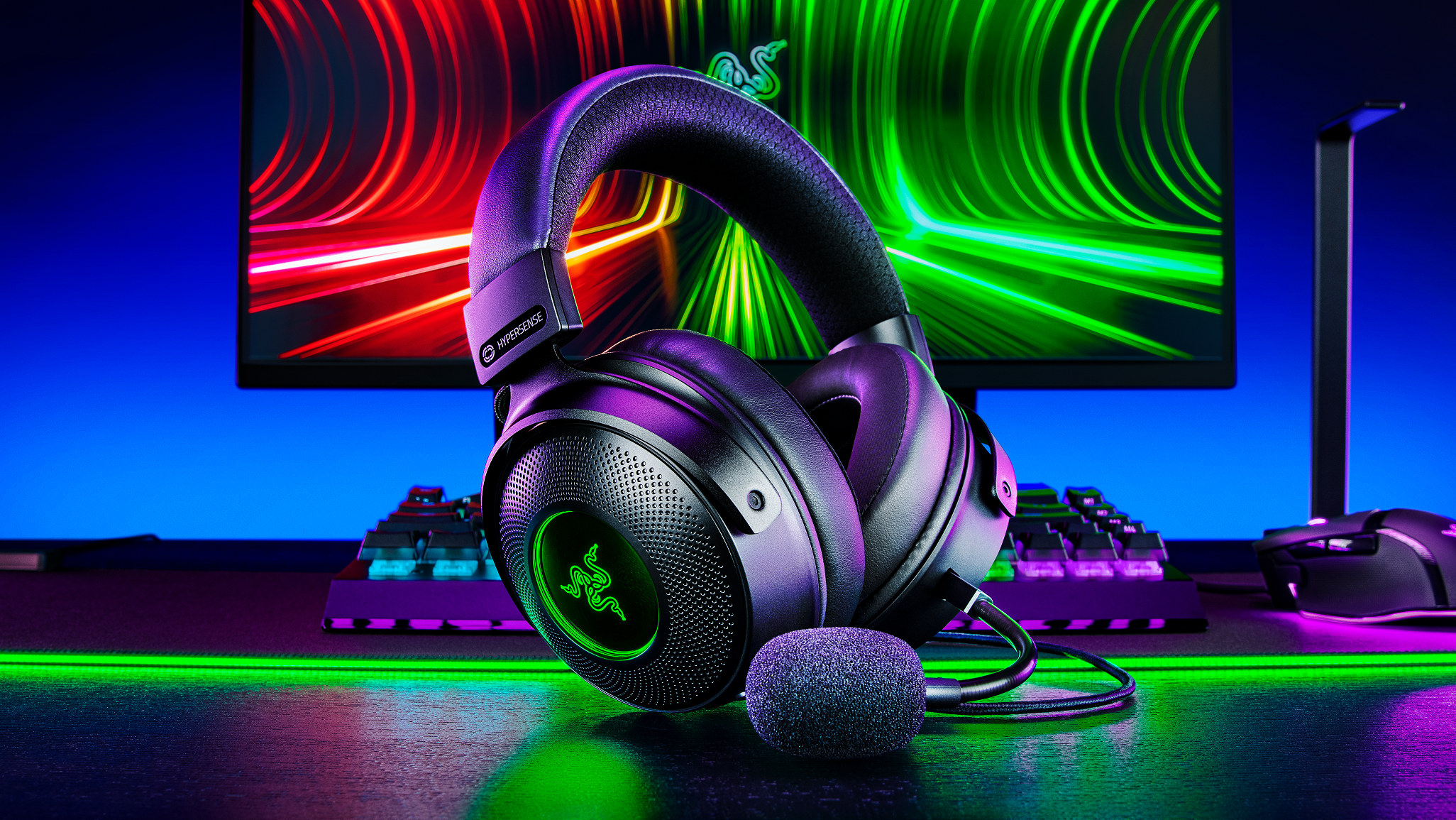 The Razer Kraken V3 HyperSense headset in front of a PC monitor and keyboard.
