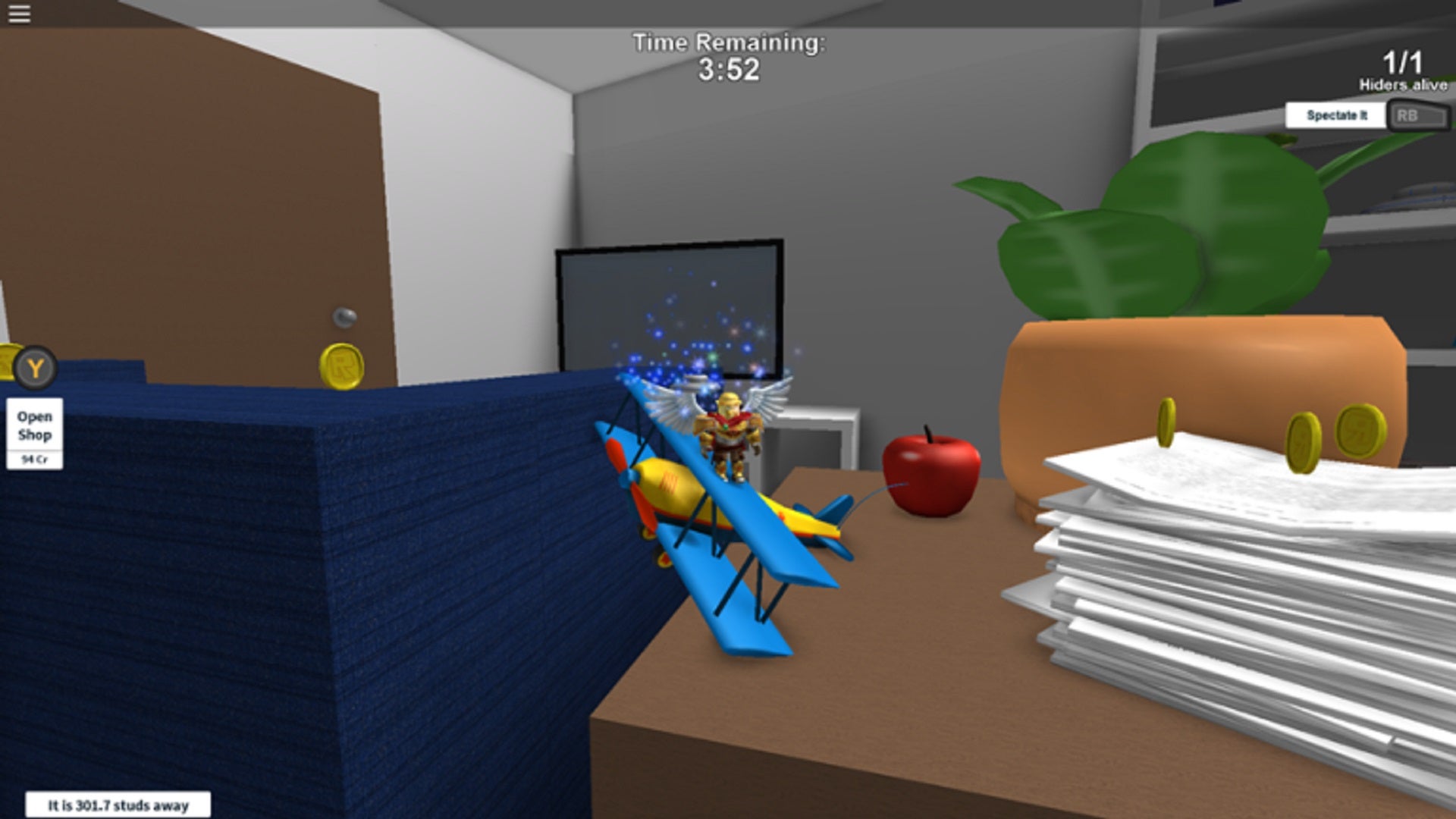 A winged Roblox character traverses a giant living room by jumping on a toy aeroplane on a table.