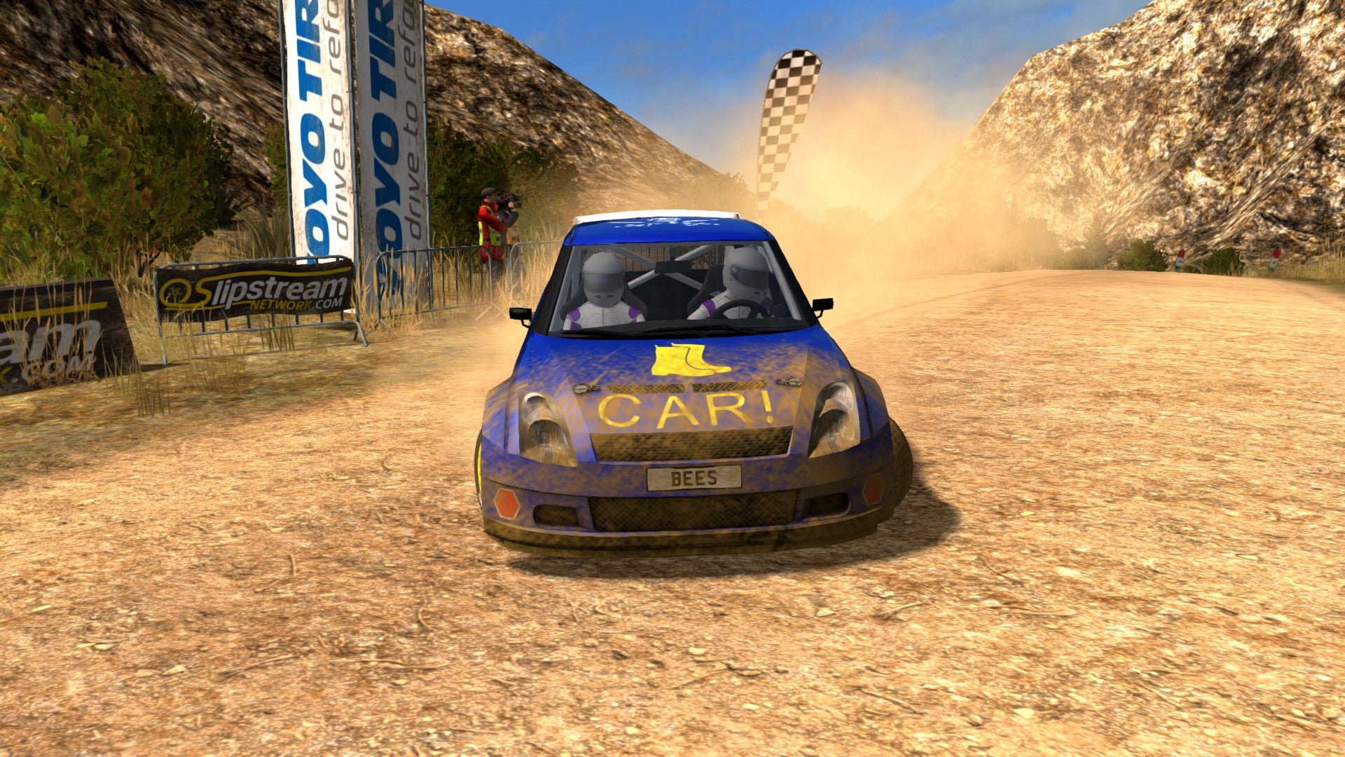 A Rush Rally 3 screenshot of blue rally car on a yellow dirt road, driving towards the camera and kicking up dust behind it