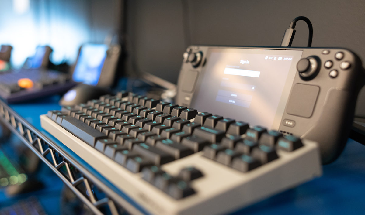 A Steam Deck dev kit stands upright, in front of a mechanical keyboard.