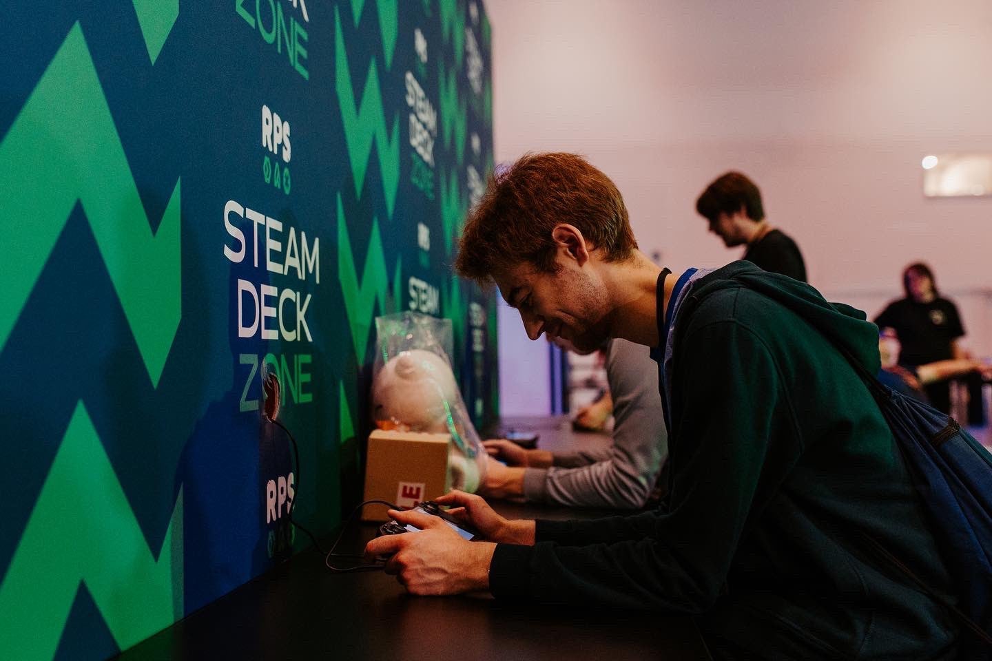 A photo of people playing Steam Decks in the RPS Steam Deck Zone at EGX London 2022.