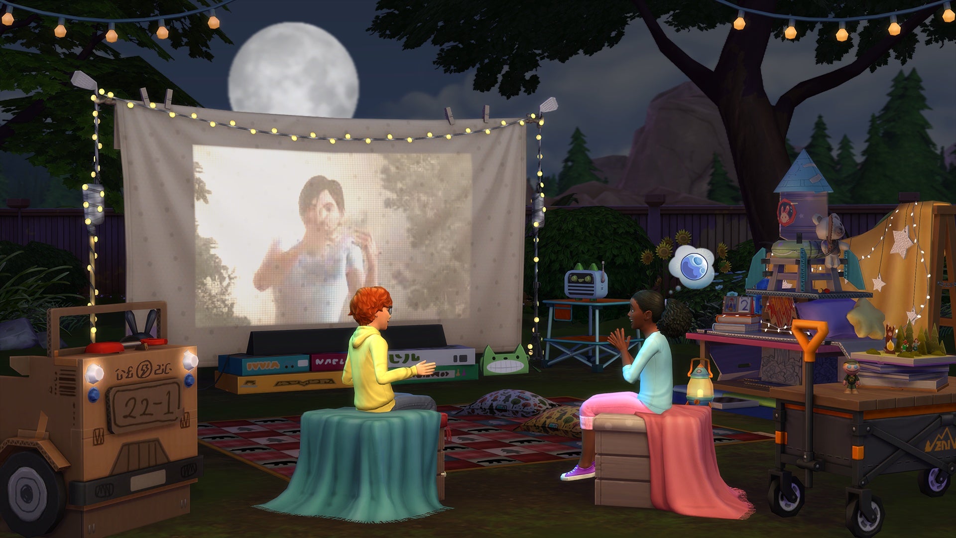 Two children in The Sims 4 sat in a back garden surrounded by outdoor camping gear in front of a sheet with a movie projected onto it at night.