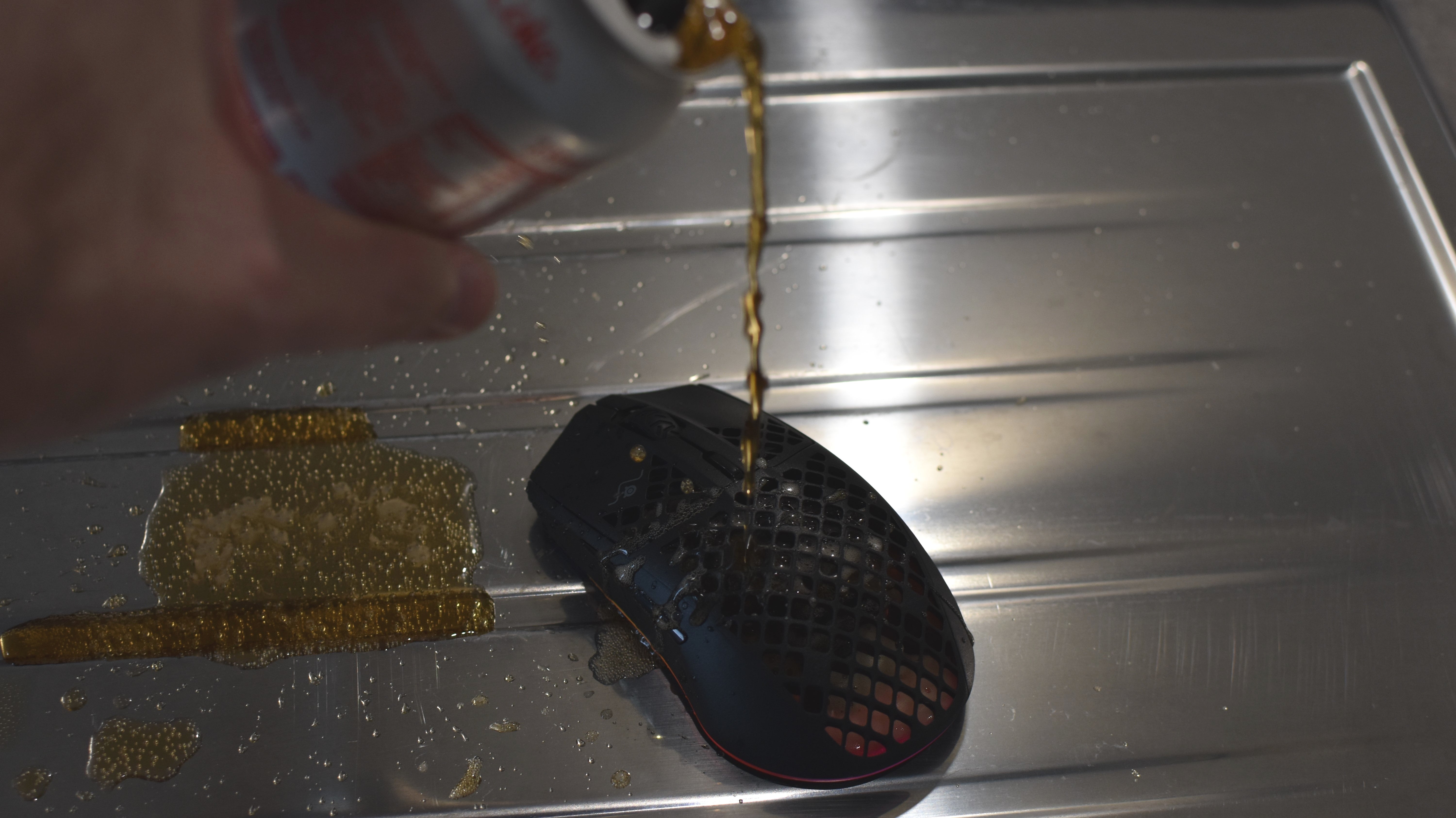 A can of Diet Coke being poured onto the SteelSeries Aerox 3 Wireless mouse, to simulate a spillage.