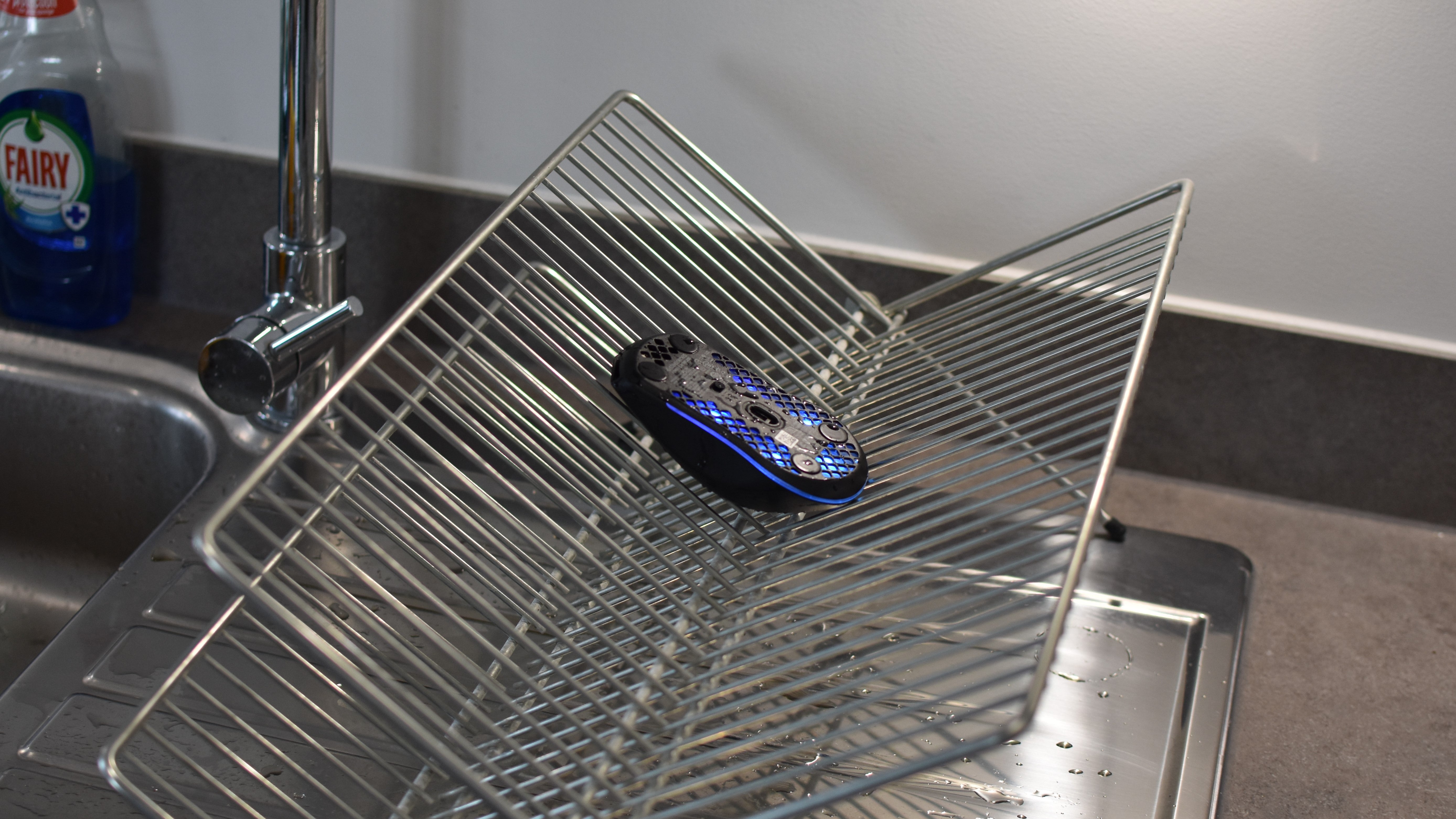 A SteelSeries Aerox 3 Wireless mouse drip-drying on a kitchen rack, having been rinsed with water.