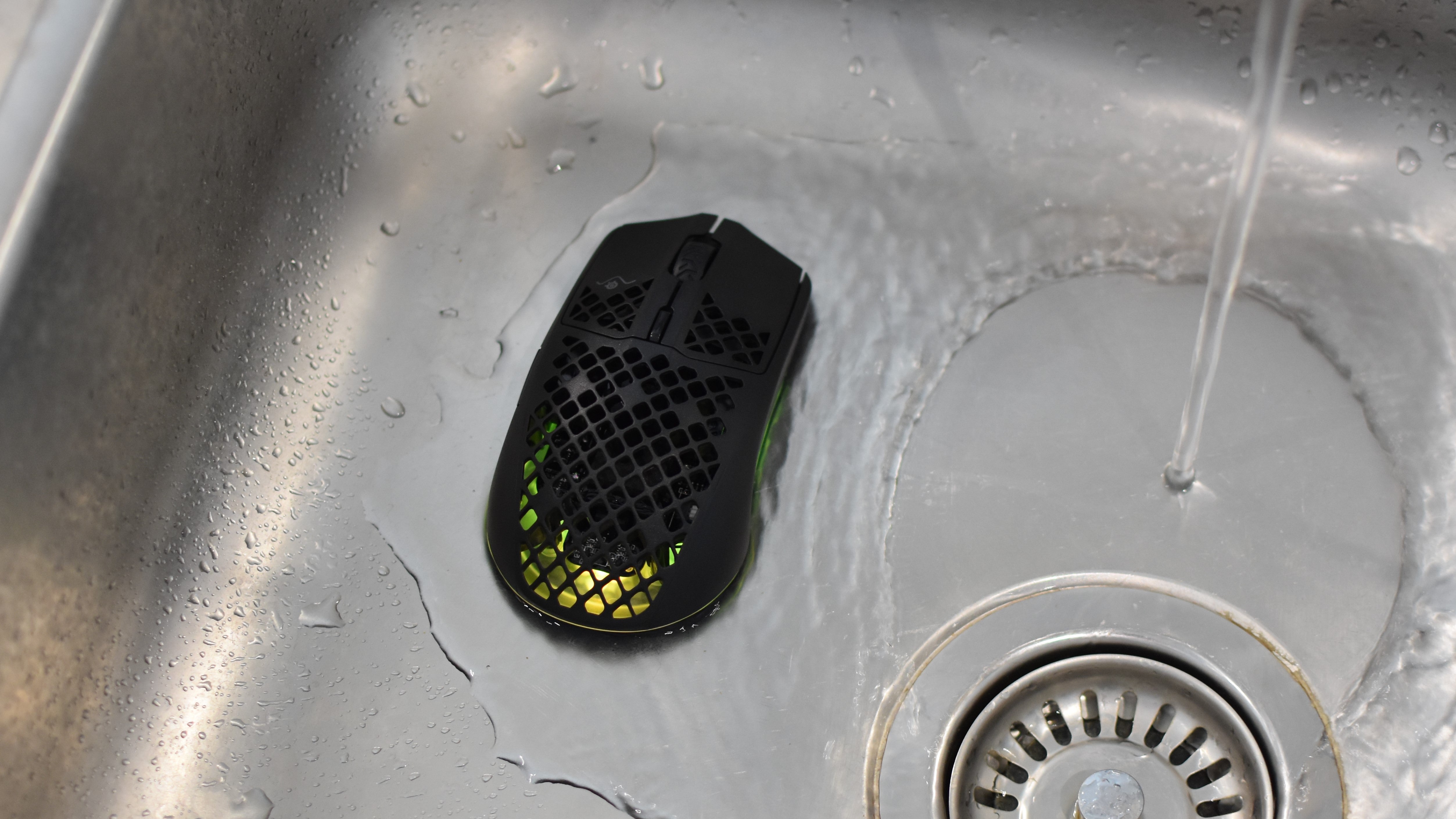 A SteelSeries Aerox 3 Wireless mouse sitting in a sink as it's surrounded by running water.