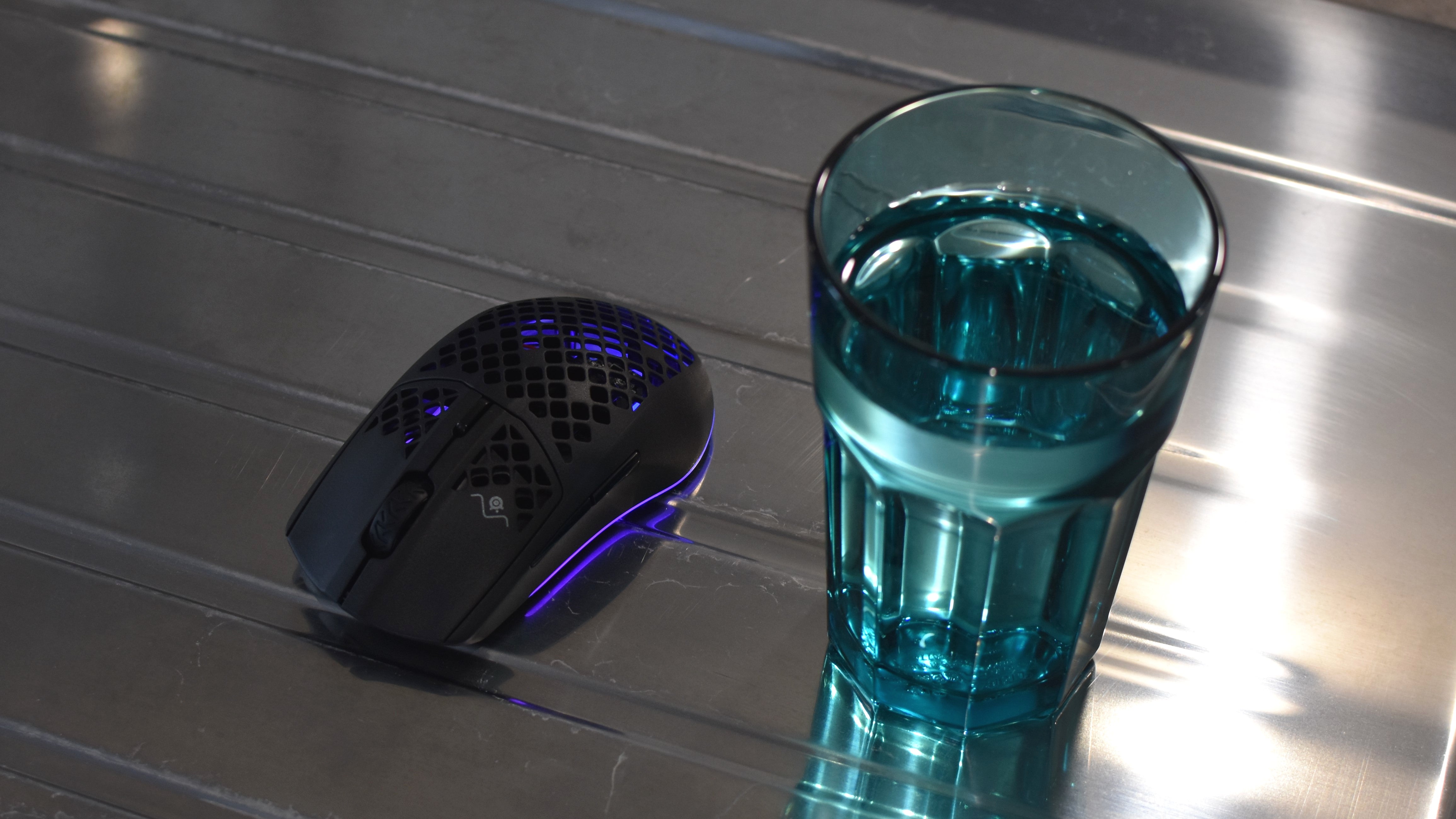 A SteelSeries Aerox 3 Wireless mouse sat next to a glass of water.