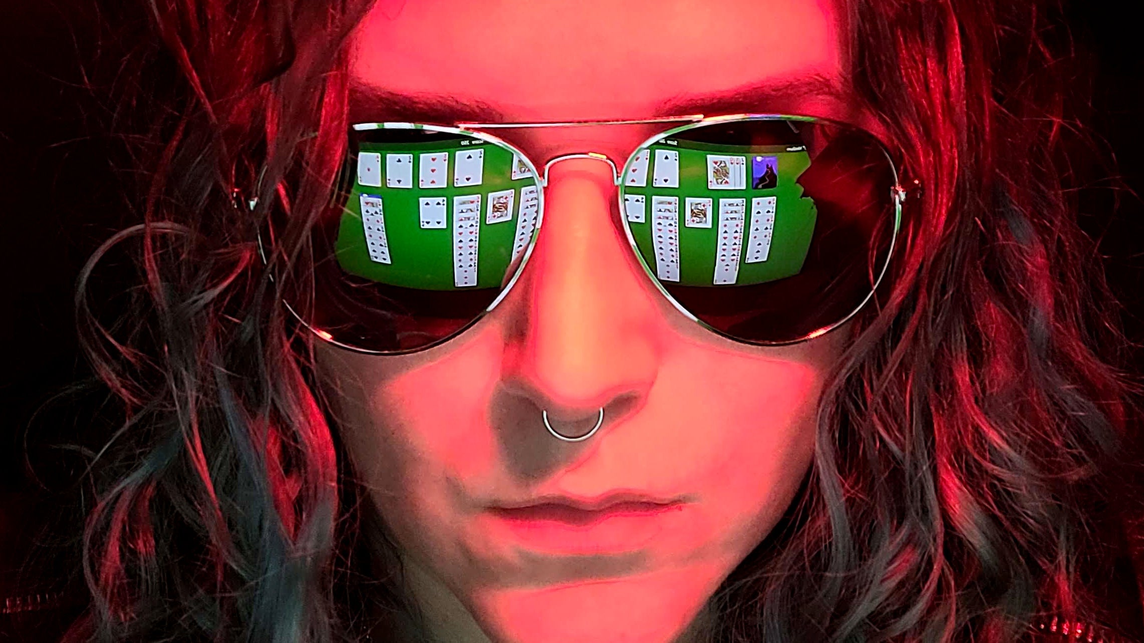 The face of a woman bathed in red light with Windows Solitaire reflected in the lenses of her mirrorshades.